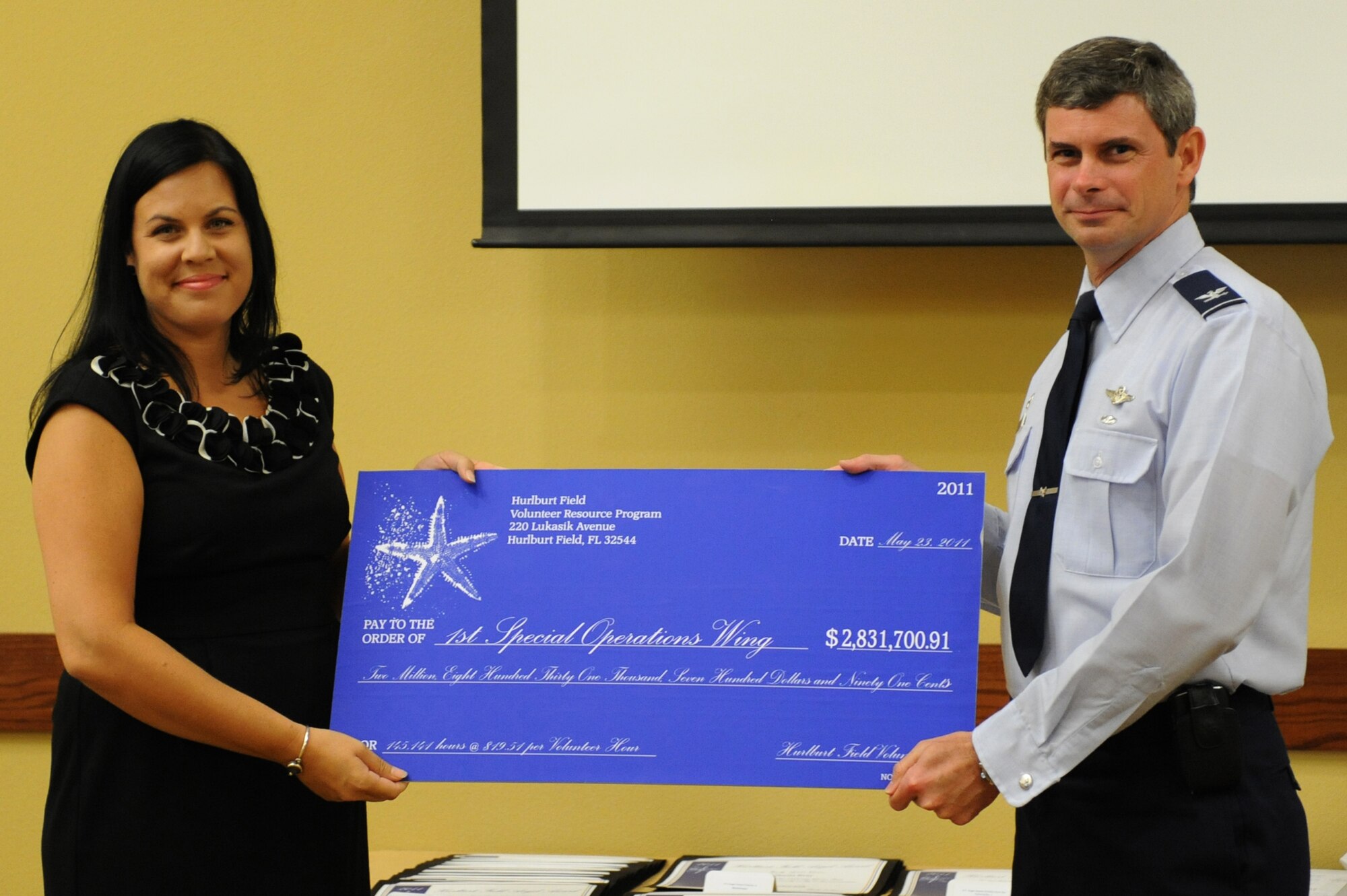Marisa Ortiz, Airman and Family Readiness Center volunteer coordinator, presents U.S. Air Force Col. Michael Plehn, 1st Special Operations Wing commander, with a check during the Volunteer Excellence and Angel Award Ceremony at the Soundside Club, Hurlburt Field, Fla., May 23, 2011. The check represents the amount of money Hurlburt Field saved by its volunteer man-hours in 2010. (U.S. Air Force photo by Airman 1st Class Caitlin O'Neil-McKeown/RELEASED) 