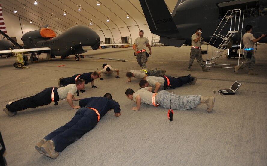 Continuing a 380th Expeditionary Aircraft Maintenance Squadron crew chief tradition, these seven execute 26 push-ups which is equivalent to this RQ-4B Global Hawk’s last two tail number digits May 11, 2011, in Southwest Asia. As in most Air Force aircraft maintenance squadrons, this is a way of christening the brand new addition to the 380th Air Expeditionary Wing. (U.S. Air Force photo by Senior Airman Maynelinne De La Cruz)     