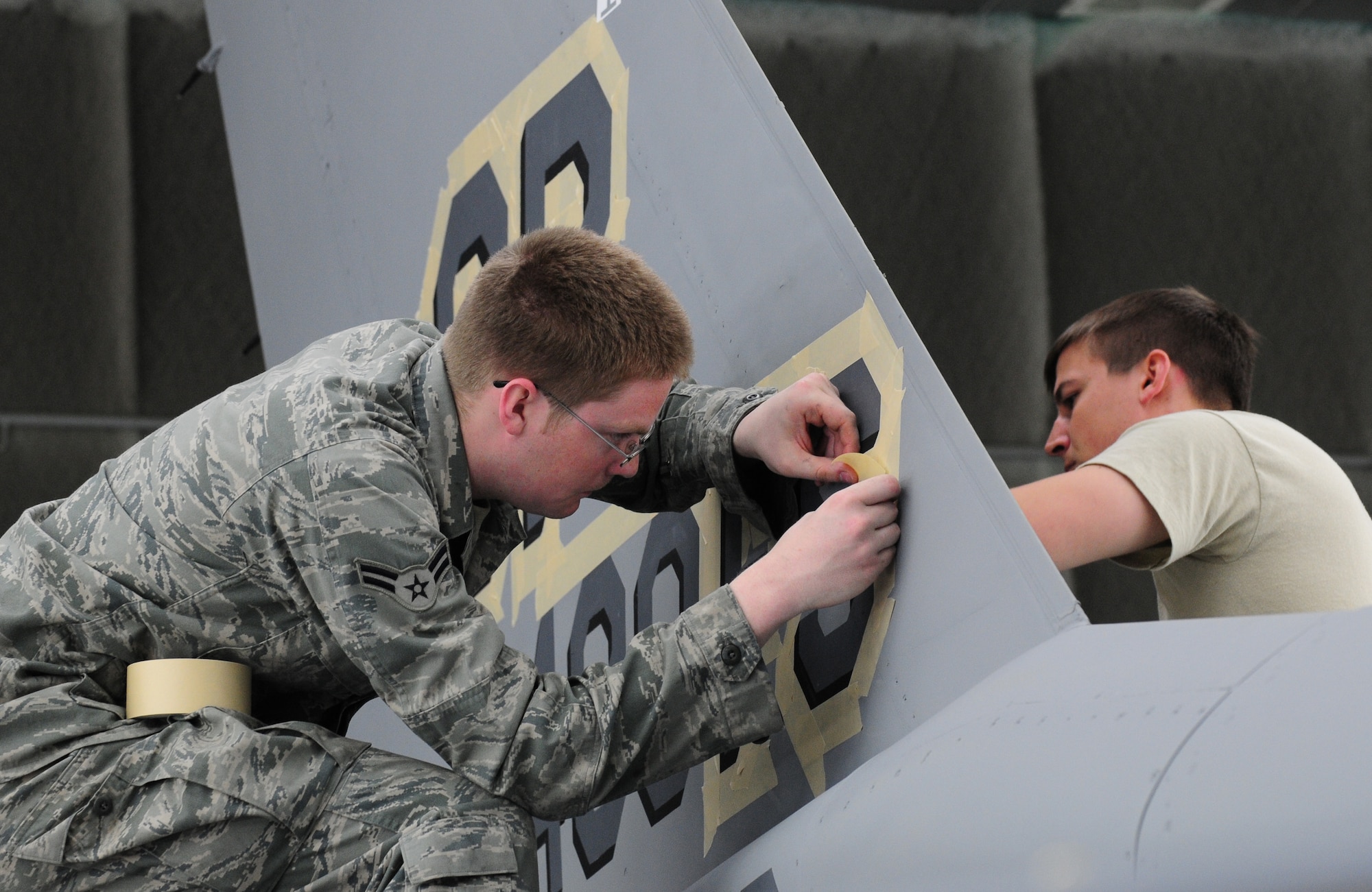 SPANGDAHLEM AIR BASE, Germany – Airman 1st Class Tyler Guttormsson and Staff Sgt. Victor Spinelli, 52nd Equipment Maintenance Squadron Fabrication Flight, apply stencils to an F-16 Fighting Falcon before painting the jet here May 16. The 52nd EMS fabrication flight works to prevent corrosion on support equipment and aircraft-related parts. (U.S. Air Force photo/Airman 1st Class Matthew B. Fredericks)