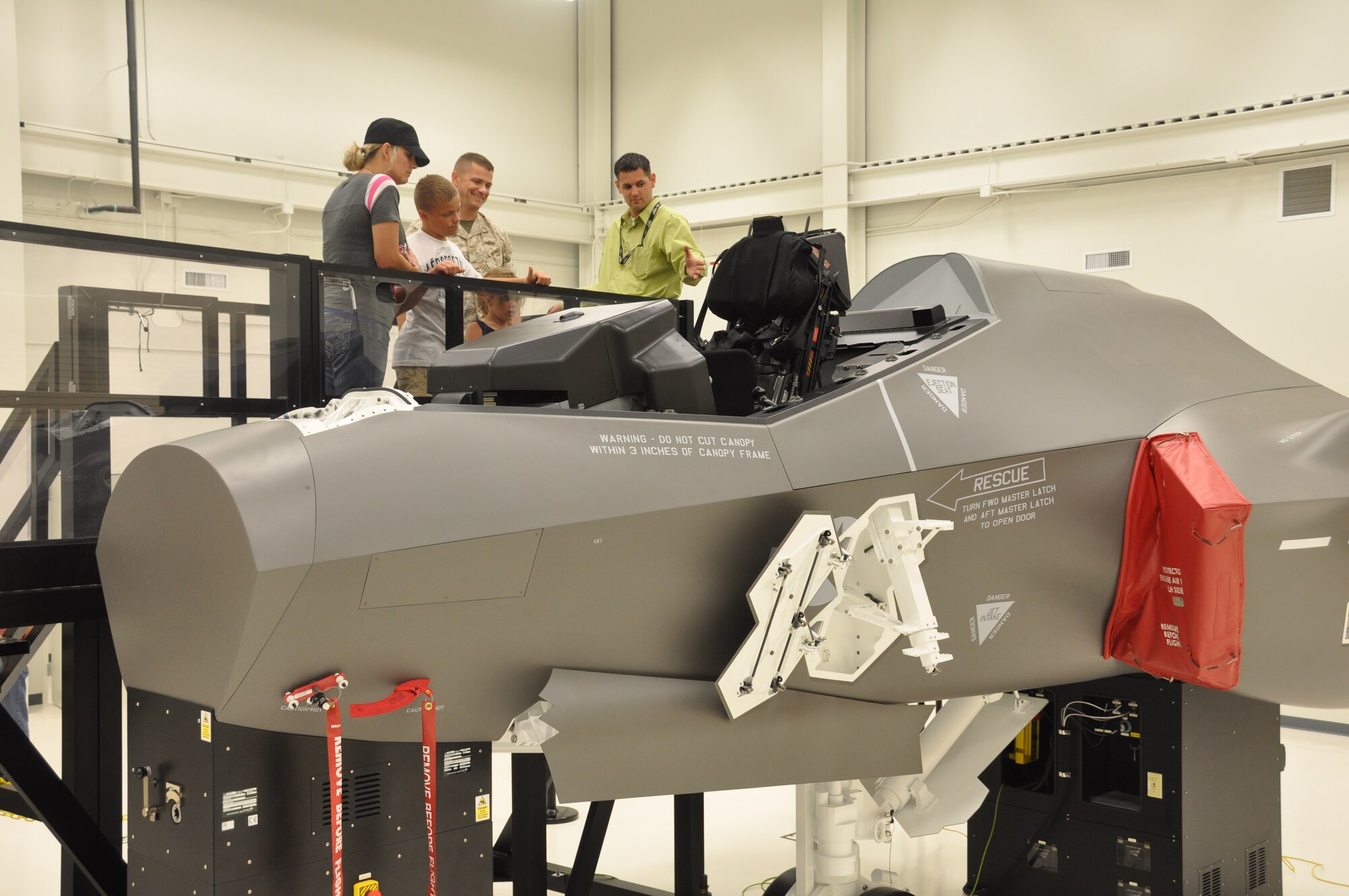 Marine Capt. Mitch Grey and his family get an up close look at the Ejection System Maintenance Trainer at the Academic Training Center during the 33rd Fighter Wing's open house for personnel and family May 27. Ron Snider, instructor, briefed the family and other visitors on how the mock cockpit will be used for training DoD's future F-35 maintainers and pilots. Leaders at the wing created the half-day itinerary followed by a picnic to showcase the unit to their integrated team and build camaraderie among themselves and contracted partners. (U.S. Air Force photo/Chrissy Cuttita)
