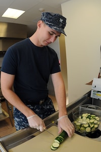 Petty Officer 3rd Class James Wring cuts zucchini at the Joint Base Charleston-Air Base Child Development Center. Wring, a machinist’s mate, is working at the JB Charleston – Air Base CDC while waiting for orders to his next school assignment. (U.S. Navy photo/Petty Officer 1st Class  Jennifer Hudson)