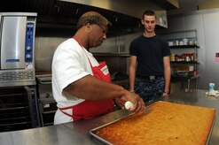 Melissa Gaines instructs Petty Officer 3rd Class Nick Nieman how to cut sweet potato bread that will be served at snack time. Nieman is working at the Joint Base Charleston Child Development Center while waiting for orders to his next school assignment. (U.S. Navy photo/Petty Officer 1st Class Jennifer Hudson)