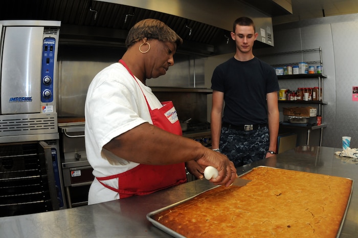 Melissa Gaines instructs Petty Officer 3rd Class Nick Nieman how to cut sweet potato bread that will be served at snack time. Nieman is working at the Joint Base Charleston Child Development Center while waiting for orders to his next school assignment. (U.S. Navy photo/Petty Officer 1st Class Jennifer Hudson)