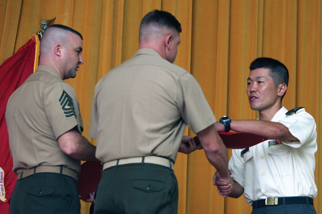 Japan Ground Self-Defense Force Sgt. Tomoshiro Nishimaki is awarded his corporals course completion certificate by Chief Warrant Officer David V. Bednarcik and 1st Sgt. Gordon M. Miller on Marine Corps Air Station Futenma Nov. 4. Nishimaki is one of the first JGSDF service members to complete a Marine Corps corporals course. Nishimaki is a gunner with the JGSDF’s 26th Infantry Regiment, Bednarcik is the division gunner of 3rd Marine Division, III Marine Expeditionary Force, and Miller is a company first sergeant with Headquarters and Service Battalion, Marine Corps Base Camp Butler.