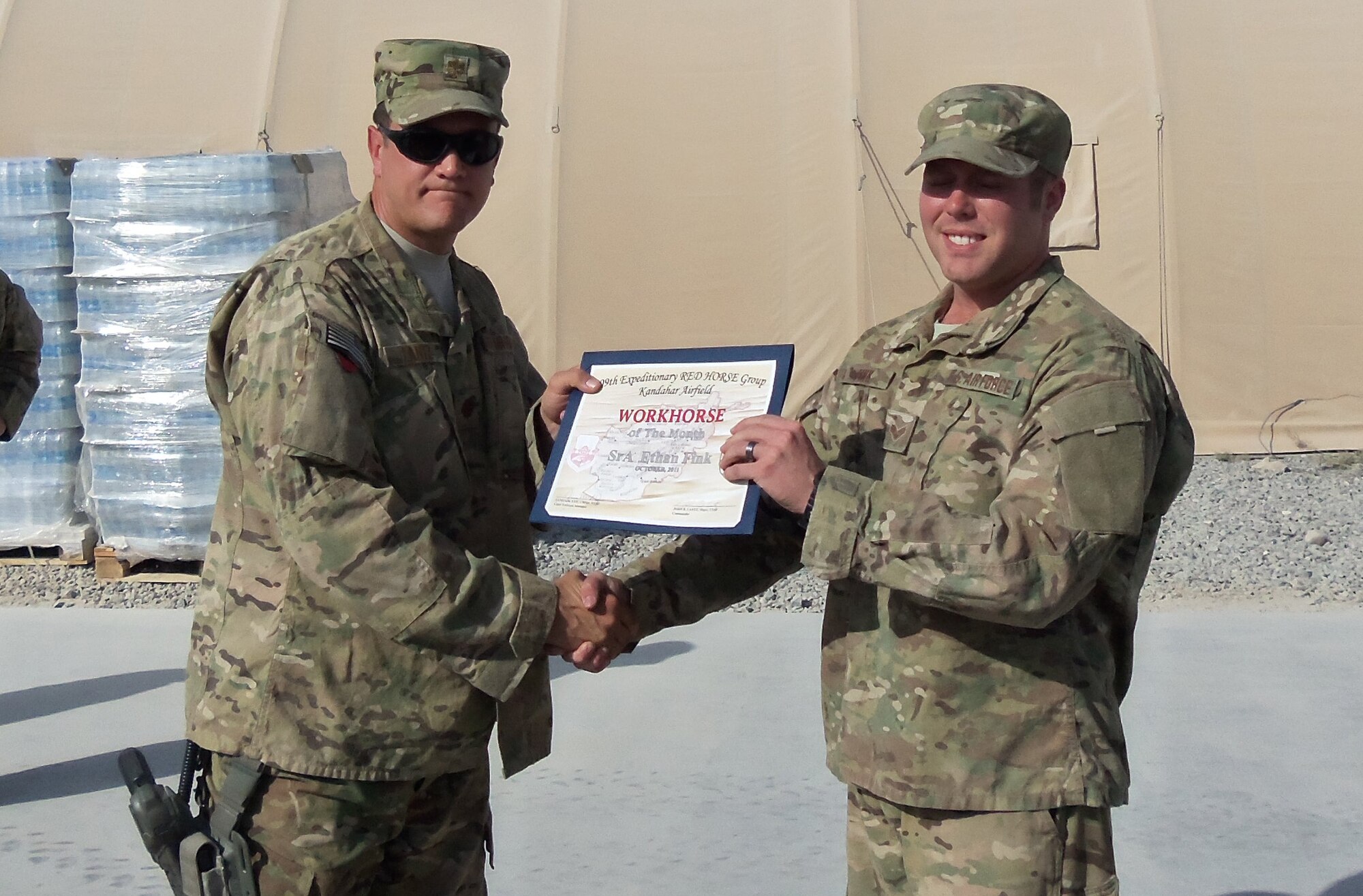 Senior Airman Ethan Fink (right), 567th RED HORSE Squadron, receives the Airman Workhorse of the Month Award while stationed at his deployed location in Aghanistan. Presenting the award is Maj. John Lantz, 809th Expeditionary RED HORSE commander. (USAF photo courtesy of 567RHS)