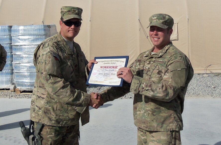 Senior Airman Ethan Fink (right), 567th RED HORSE Squadron, receives the Airman Workhorse of the Month Award while stationed at his deployed location in Aghanistan. Presenting the award is Maj. John Lantz, 809th Expeditionary RED HORSE commander. (USAF photo courtesy of 567RHS)