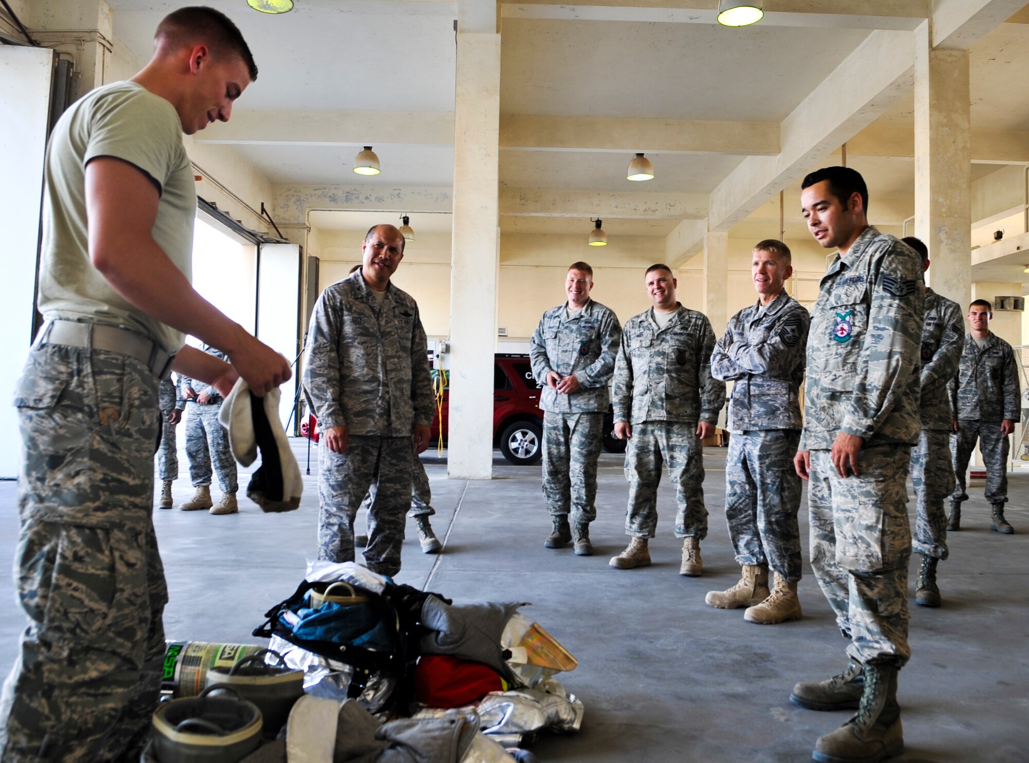 Airman 1st Class Alec Ribbink (left), 379th Civil Engineer Squadron firefighter, shows Col. Giovanni Tuck (second from left), 379th Air Expeditionary Wing commander, how to don a protective mask before putting on aluminized proximity gear Nov. 2, 2011, at an undisclosed location in Southwest Asia. The commander makes frequent visits, called “Day in the Shoes,” to units around the base to get a firsthand look at Airmen and their missions. Ribbink, a native of Daytona Beach, Fla., is deployed from Grand Forks Air Force Base, N.D. (U.S. Air Force photo/Senior Airman Paul Labbe)