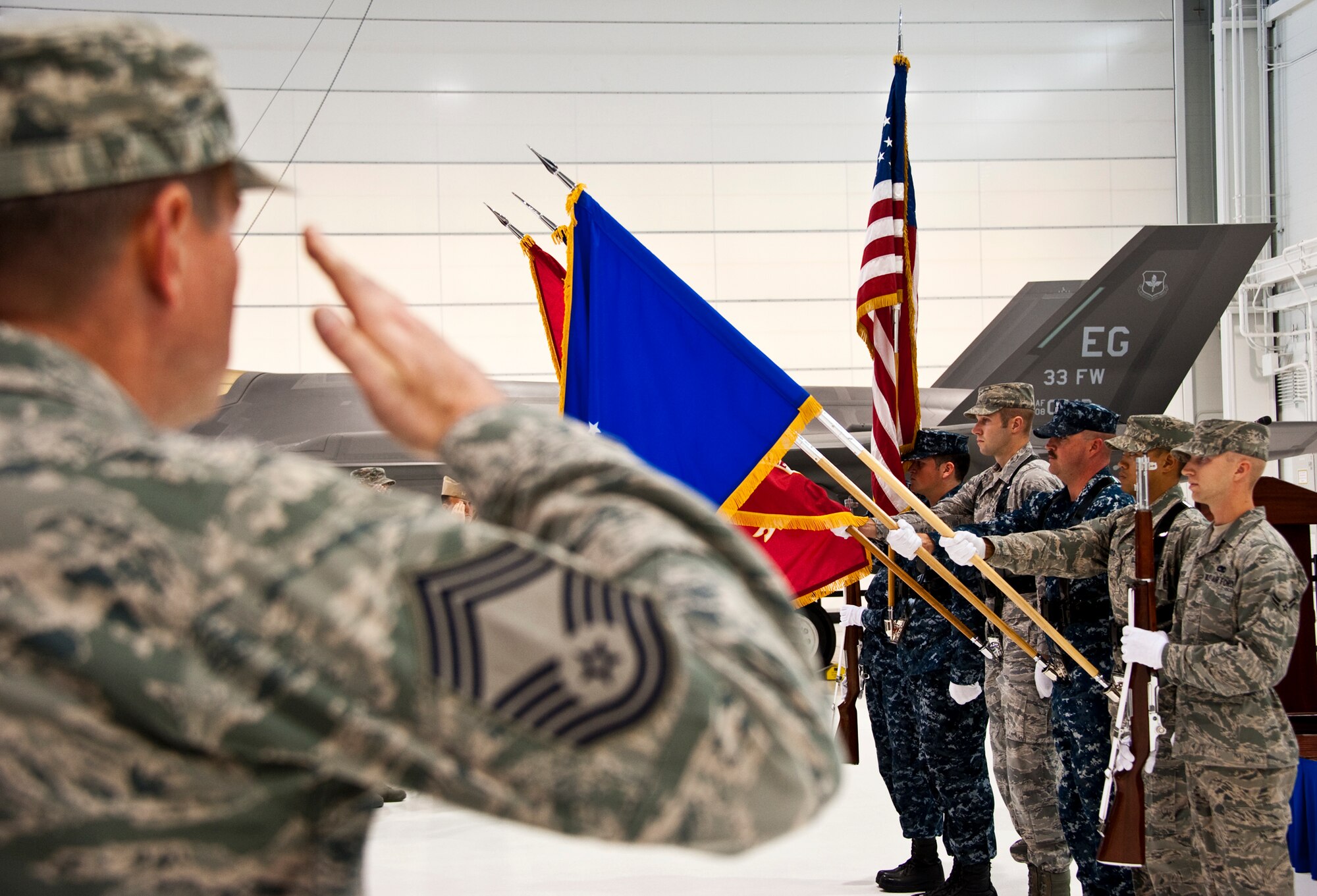 A chief master sergeant salutes as the newly-formed joint color guard team of 33rd Fighter Wing members presents the colors for the first time during a recent change of command ceremony at Eglin Air Force Base, Fla., Nov. 2. The joint color guard team members are:  Corpsman Sarah Lambert, Petty Officer 2nd Class James Peters, Senior Airman Chad Walker, Petty Officer 1st Class Jack Bauer, Master Sgt. Alexander Fortunato and Airman 1st Class Justin Glover.  (U.S. Air Force photo/Samuel King Jr.)