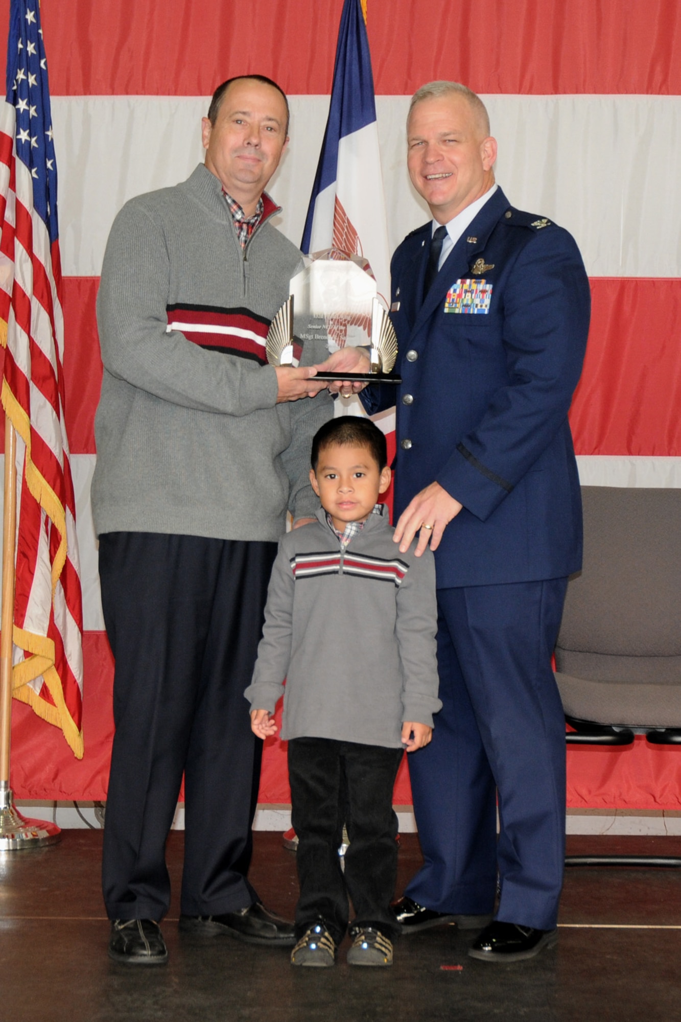 Col. Drew DeHaes (right) presents Mark (left) and Trent Safranski (middle), husband and son of Master Sgt. Brenda Safranski, with the Senior NCO of the Year award during the 2011 Awards Ceremony held in the hangar of the 132nd Fighter Wing, Des Moines, Iowa on November 6, 2011.  MSgt. Safranski is currently on temporary duty assignment (TDY); Mark and Trent accept on her behalf.  (US Air Force photo/Staff Sgt. Linda E. Kephart)(Released)