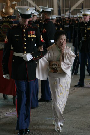 Cpl. Matthew L. E. Doyle, Marine Aviation Logistics Squadron 12 community relations coordinator, escorts Machiko Hamamoto, Honorary Marine recipient, during an award ceremony at the Strike Fighter Squadron 94 hangar here Tuesday. The title of Honorary Marine is an award bestowed on::r::::n::civilians who have made extraordinary contributions to the Marine Corps. The award is approved solely by the Commandant of the Marine Corps. Hamamoto, 82, has spent 43 years working alongside Marines, organizing cleanup and community relations projects. She also collects Christmas gifts::r::::n::for local handicapped children and for children at Shobara Sakura Gakuen orphanage. Her helping hand has reached even to the U.S. She received an American Red Cross certificate of appreciation for her role in delivering Red::r::::n::Cross services after the 1989 Loma Prieta earthquake near San Francisco.