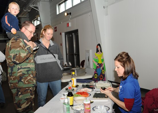 U.S. Navy Cmdr. Anthony Tranchita, 319 MDOS Group, watches Leah Melquist, base Health Promotion Manager, roll sushi for a display booth at the Multicultural World Showcase on Nov. 9 on Grand Forks Air Force Base, N.D.  Members of the Grand Forks military community gathered to celebrate their diversity with educational booths, dance and music demonstrations and food from around the world.  (U.S. Air Force photo by Airman 1st Class Ashley N. Taylor)