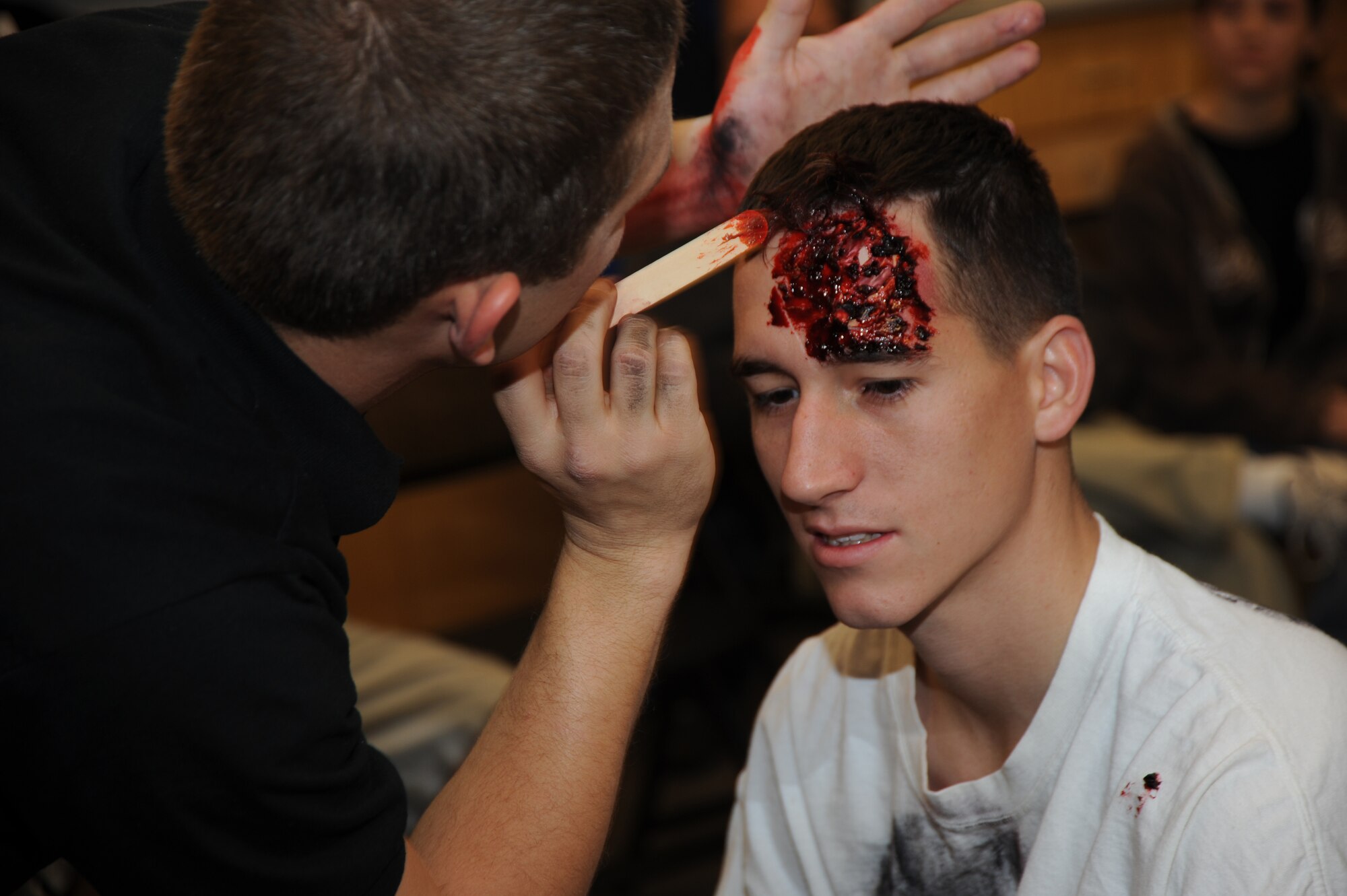 U.S. Air Force Airman 1st Class Michael Abrams, 355th Civil Engineer Squadron firefighter, sits in the moulage room as Mr. Daniel Veres, Pima Community College emergency medical technician, creates a simulated head wound on his forehead at the Tucson Metropolitan Medical Response Systems exercise held in Tucson, Ariz., Nov. 10, 2011. Abrams was one of approximately 65 Airmen from Davis-Monthan Air Force Base who volunteered for the medical exercise. (U.S. Air Force photo by Airman 1st Class Saphfire Cook/Released)