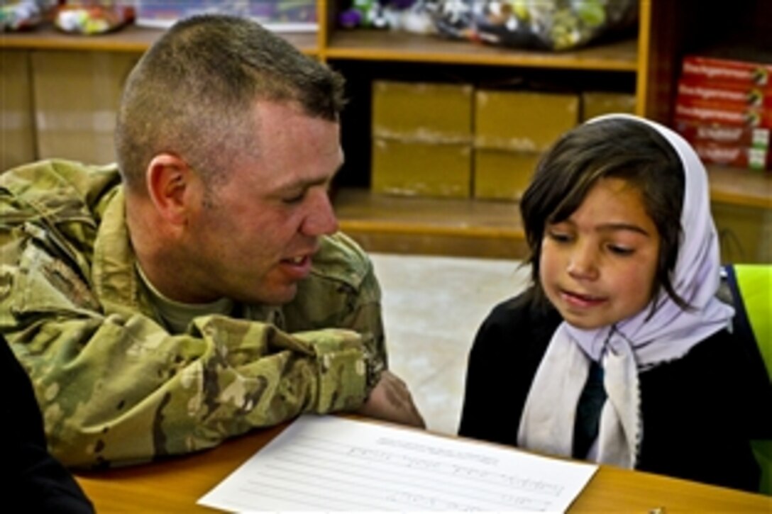 U.S. Air Force Master Sgt. James Wooding assists an Afghan girl with her classwork at The Cat in the Hat Language Arts Center, a new school on Bagram Airfield, Afghanistan, Nov. 13, 2011. The U.S. Army runs the school, which helps teach students English.