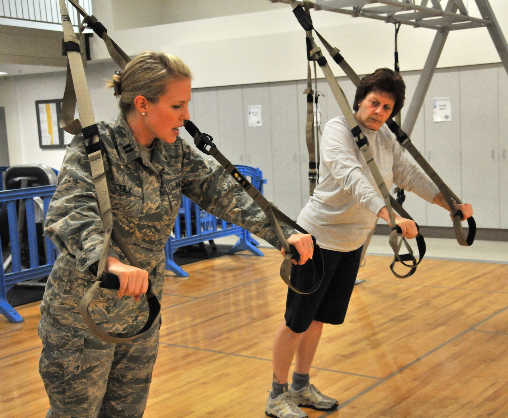Capt. Carrianne Culy, 446th Airlift Wing fitness program manager, demonstrates the proper rowing form on the TRX suspension straps to Senior Master Sgt. Liz Milligan, superintendent, 446th Operations Support Flight at the Fitness Annex here Nov. 15, 2011.  Milligan, a longtime Reservist, took Culy up on her challenge and tested the new fitness equipment after conquering miles of hills during her usual lunchtime cycling class.