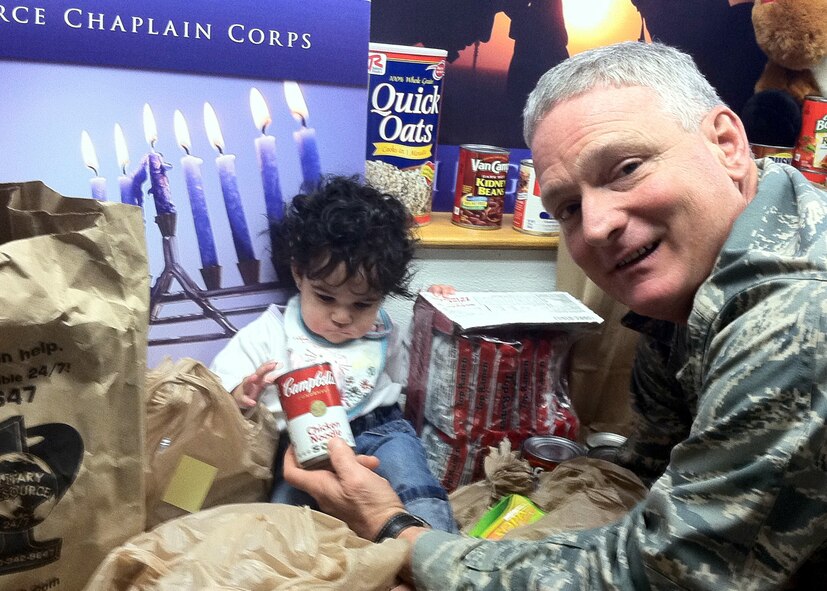TRAVIS AIR FORCE BASE, Calif. -- The 349th Air Mobility Wing Holiday Food Drive is underway. Here, Chaplain (Col.) Tyler Guy, 349th Air Mobility Wing chief chaplain, gets a helping hand from Margaret Ann Sullivan, five month old daughter of Staff Sgt. Kenyetta King, chaplains assistant. The 349th AMW chaplain corps sponsors the annual drive to feed those in need in Solano County and within our Air Force family. There are decorated barrels throughout the wing in various locations for dropping off non-perishable food items, or stop by the Chaplains Office, and they can take your donation. The drive ends Dec. 15, in time to distribute the food for the holidays. (U.S. Air Force photo/Master Sgt. Rita Houchin).