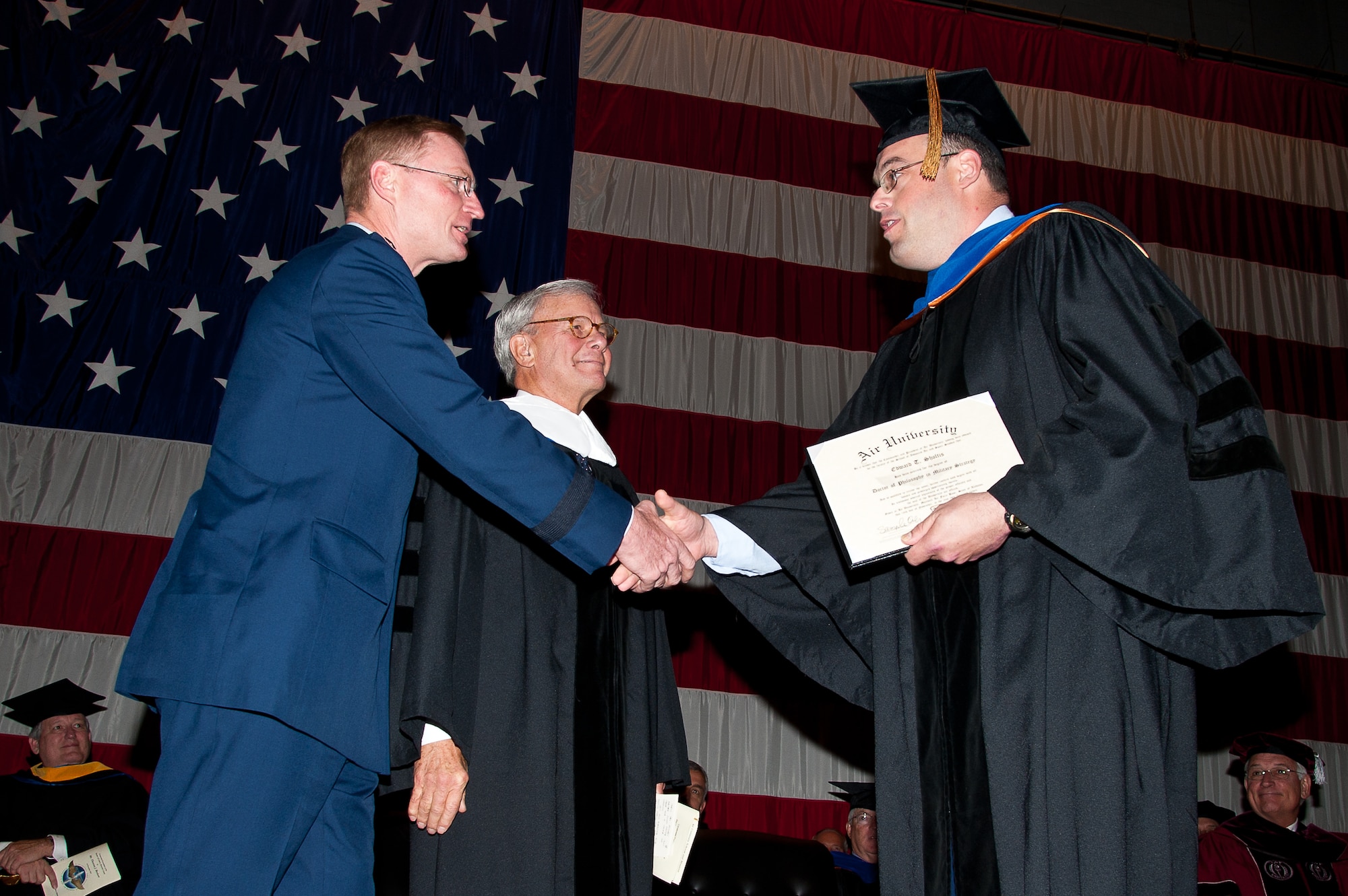 Lt. Col. Tadd Sholtis, right, deputy director of public affairs at Headquarters Air Combat Command at Langley AFB, Va., is presented the Air University's first Maxwell-conferred doctorate degree Monday by Lt. Gen. David Fadok, right, as AU honorary degree recipient Tom Brokaw looks on. (Air Force photo/Melanie Rodgers Cox)