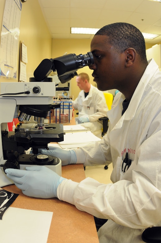 Petty Officer 3rd Class Kendrick Minion looks at a bacteria slide through a microscope while Petty Officer 3rd Class Matthew Hampton (back) visually identifies a growing bacterium in a petri-dish. The microbiology lab allows hospital corpsmen to look at a blood smear on a petri-dish, visually looking for growing bacteria and then look at it again for verification through a microscope. The final step is to put the sample through a microbiology analyzer machine which is able to identify the type of infection and can identify which antibiotics can be used to kill it. Both Minion and Hampton are Hospital Corpsmen at Naval Health Clinic Charleston. (U.S. Navy photo/Petty Officer 1st Class Jennifer Hudson)