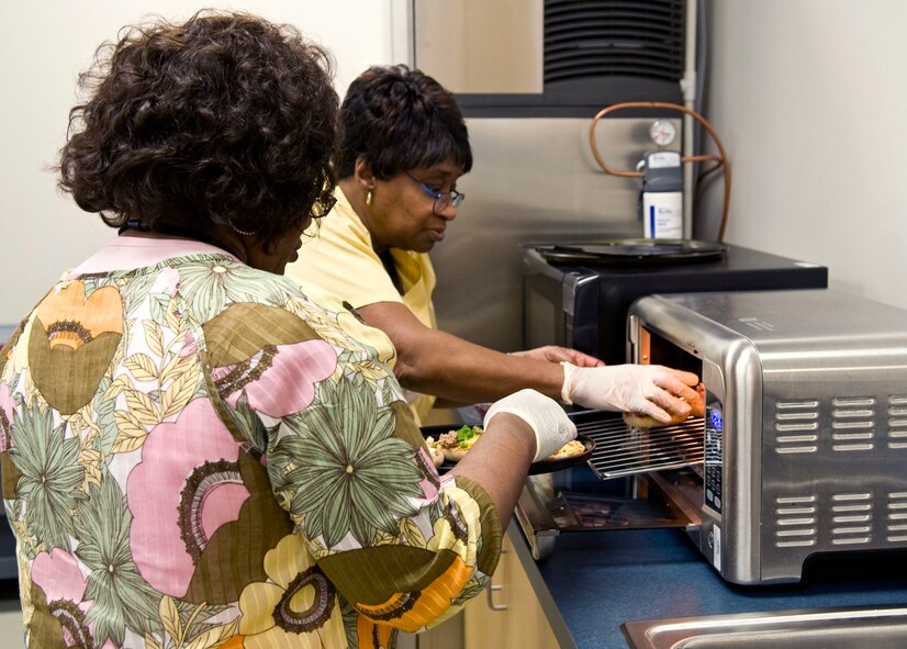 Wanda Murray, front, and Frankie Canty put pizza inside a toaster oven at the Northwest Louisiana War Veterans home in Bossier City, La., Nov. 15. Murray and Canty work for the veterans home and help organize and run events for residents. (U.S. Air Force photo/Airman 1st Class Benjamin Gonsier)(RELEASED)