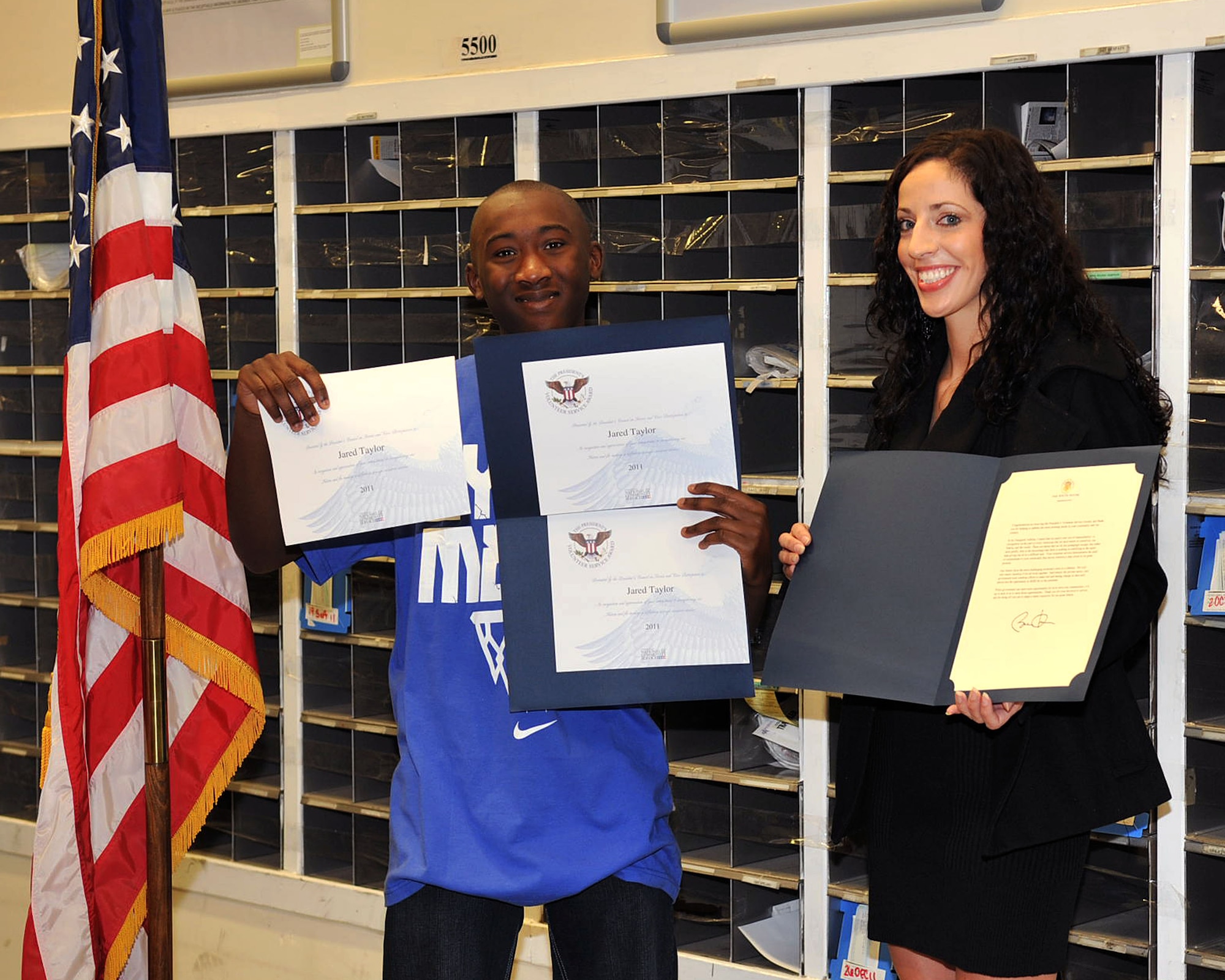 RAF MILDENHALL, England - Kari Rosett, right, 100th Force Support Squadron teen coordinator, presents three Presidential Volunteer Service Award certificates to Jared Taylor, 15, at the post office here Nov. 10, 2011. Taylor earned the bronze, silver and gold level awards for contributing more than 260 volunteer service hours in the last 15 months to the base post office. (U.S. Air Force photo/Senior Airman Jerilyn Quintanilla)