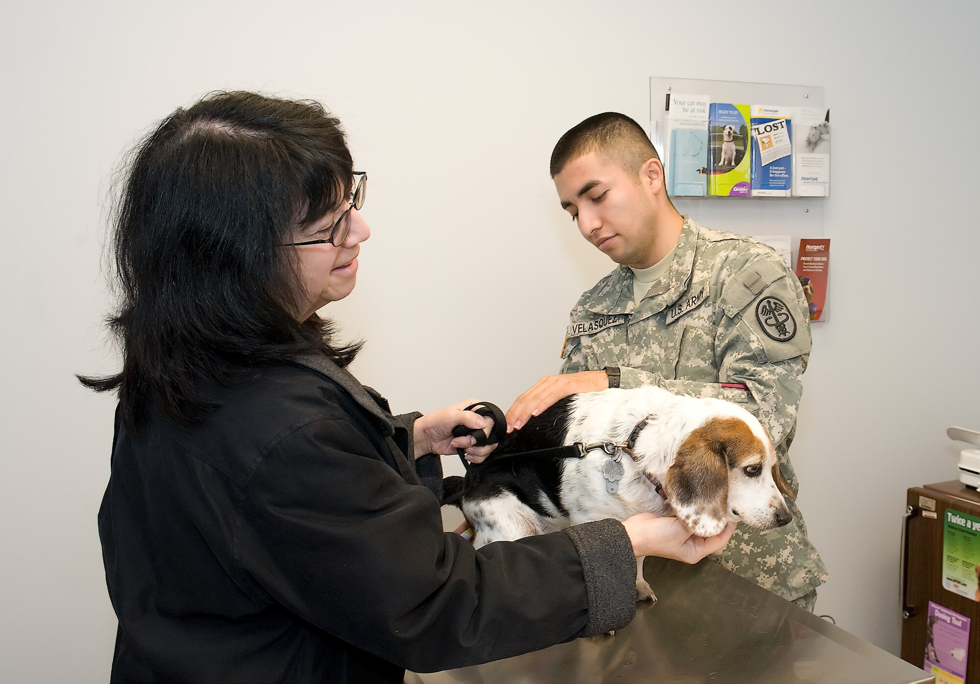 Dee Adriance (left) comforts Daisy while Army private first class Hector Velasquez, animal care specialist for the Dover Air Force Base, Del., veterinary clinic, performs a check-up. It is important to ensure animals are healthy prior to the winter season, as many health issues can be aggravated due to the extreme temperatures. (U.S. Air Force photo by Steve Kotecki)