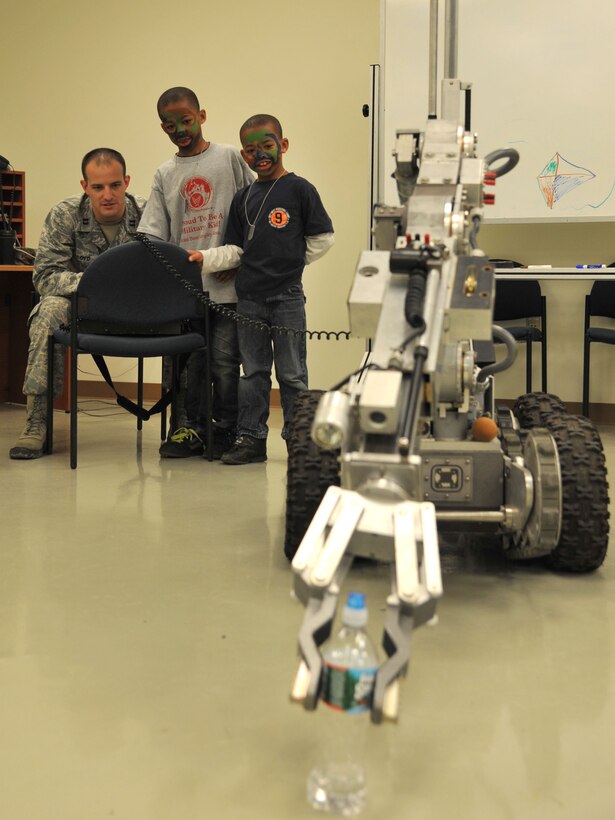 Xavier and Frank Woods, sons of U.S. Air Force Tech Sgt. Frank Woods, watch as U.S. Air Force Capt. Curtis Lloyd, 633rd Explosive Ordnance Disposal flight commander, demonstrates the EOD robot during Operation Hero at Langley Air Force Base, Va., Nov. 19, 2011. Operation Hero provides fun and entertainment for children, while also allowing them to experience elements of the deployment processing line, as their parents experience it.  (U.S. Air Force photo by Airman 1st Class Camilla Griffin/Released)