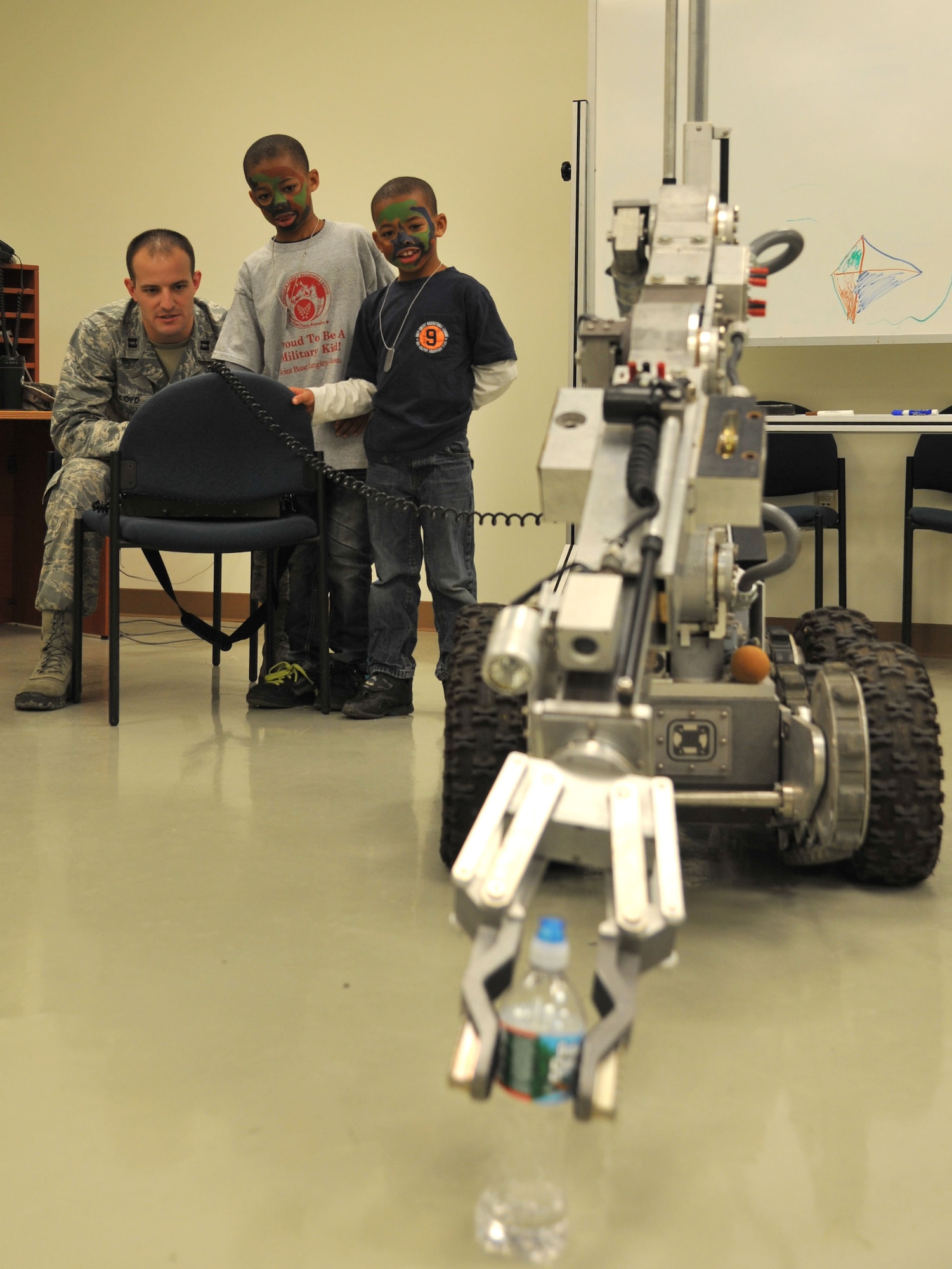 Xavier and Frank Woods, sons of U.S. Air Force Tech Sgt. Frank Woods, watch as U.S. Air Force Capt. Curtis Lloyd, 633rd Explosive Ordnance Disposal flight commander, demonstrates the EOD robot during Operation Hero at Langley Air Force Base, Va., Nov. 19, 2011. Operation Hero provides fun and entertainment for children, while also allowing them to experience elements of the deployment processing line, as their parents experience it.  (U.S. Air Force photo by Airman 1st Class Camilla Griffin/Released)
