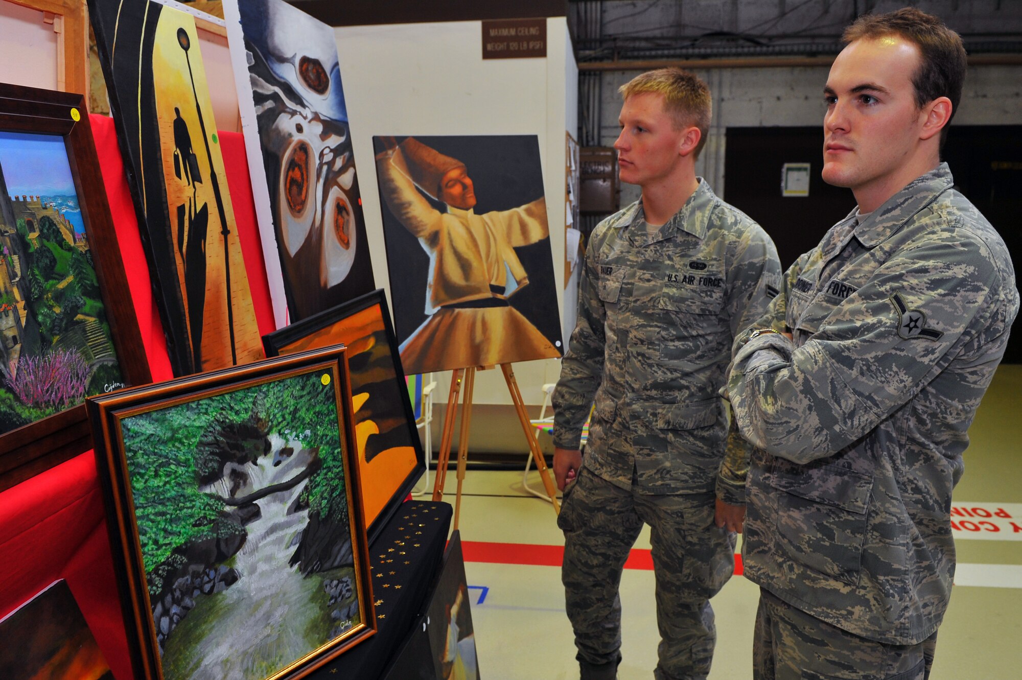 SPANGDAHLEM AIR BASE, Germany – Airman 1st Class Miles Bauer, 606th Air Control Squadron, and Airman Steven Marrinier, Armed Forces Network Spangdahlem, look at paintings at the fall bazaar here Nov. 18. The Officer and Civilian Spouses Club hosts the bazaar annually, allowing vendors from across Europe to share their products with military members and their families. These products included foodstuffs, furniture and traditional German décor. (U.S. Air Force photo/Airman 1st Class Dillon Davis)