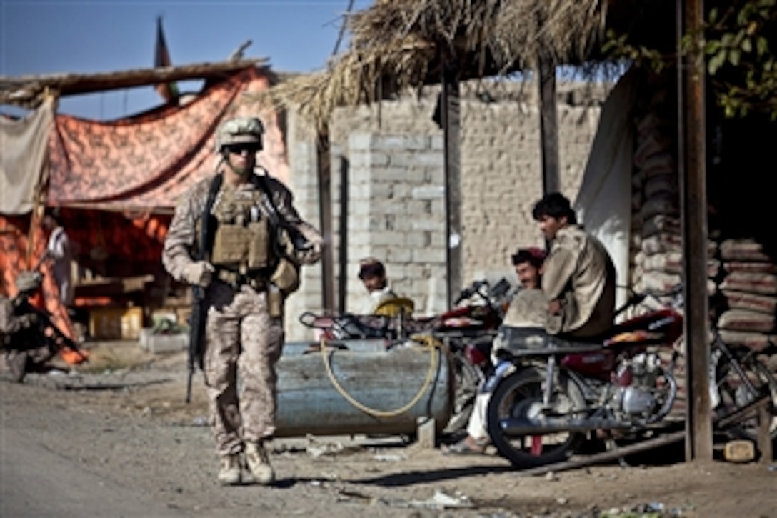 U.S. Marine Lance Cpl. Kevin Jones walks past a group of Afghan citizens during a security patrol in the Garmsir district of Helmand province, Afghanistan, on Nov. 12, 2011.  Jones is a combat photographer assigned to Headquarters and Service Company, 3rd Battalion, 3rd Marine Regiment.  