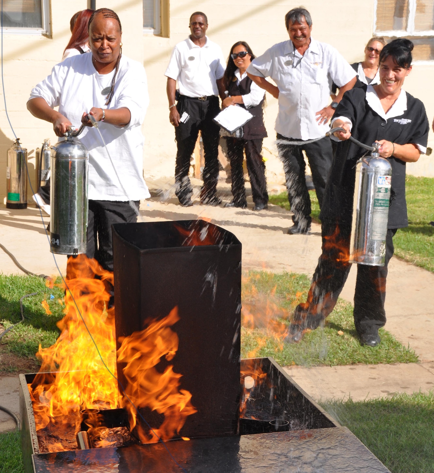 Anita Richardson (left), a March Inn room attendant, and Maria Pedraza, March Inn housekeeping, use fire extinguishers to battle a blaze in the backyard of a Gilley House, at March Air Reserve Base, Calif., Oct. 11, 2011. The extinguisher training was a part of the March Fire Department’s Fire Prevention Week outreach activities. (U.S. Air Force photos/Staff Sgt. Megan Crusher)