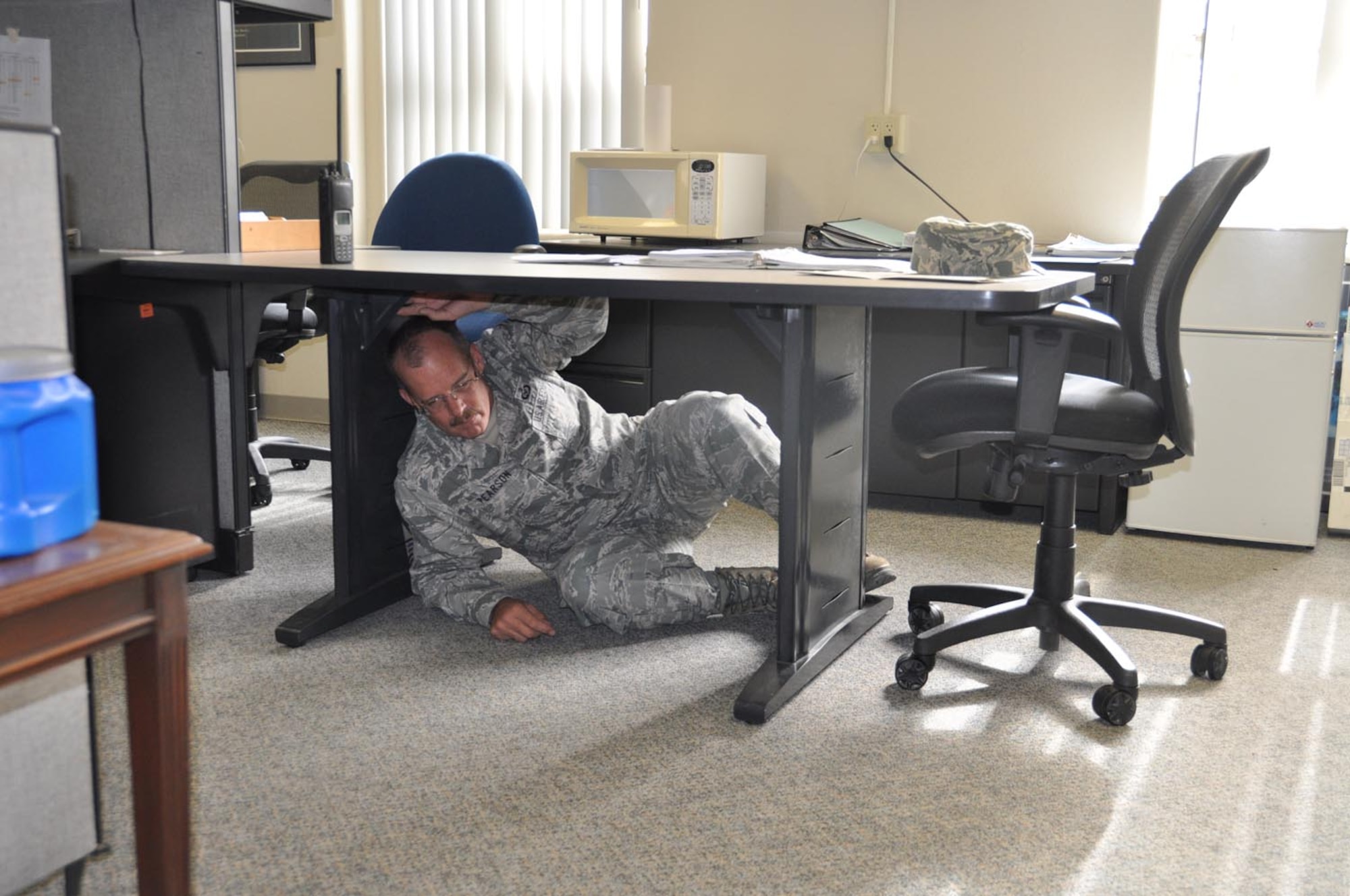 During the California-wide Great ShakeOut earthquake drill, Chief Master Sgt. Dennis Pearson, 4th Air Force, takes cover under a table in his office at March Air Reserve Base, Calif., Oct. 20, 2011. (U.S. Air Force photos/Lt. Col. Don Traud)