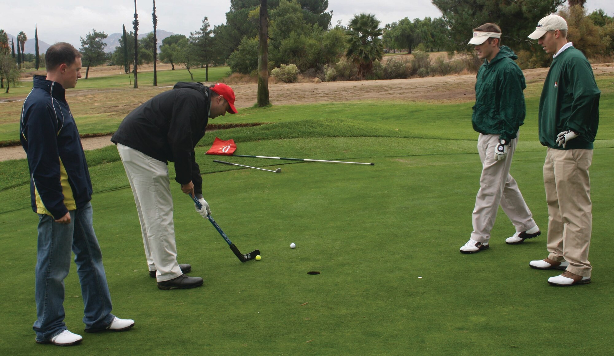Captains Joshua Chambers, Thomas Bockrath and Rick Adams, all of the 912th Air Refueling Squadron, watch Capt. James Studer use a hockey stick to putt a golf ball into the hole at the General Old Golf Course, adjacent to March Air Reserve Base, Calif., Nov. 4, 2011. The use of non-standard putting tools was an element of the squadron's fundraising tournament. Other putting tools included a tennis racket, cue stick and a baseball bat. (U.S. Air Force photo/Staff Sgt. Sara Margaret E. Luna)