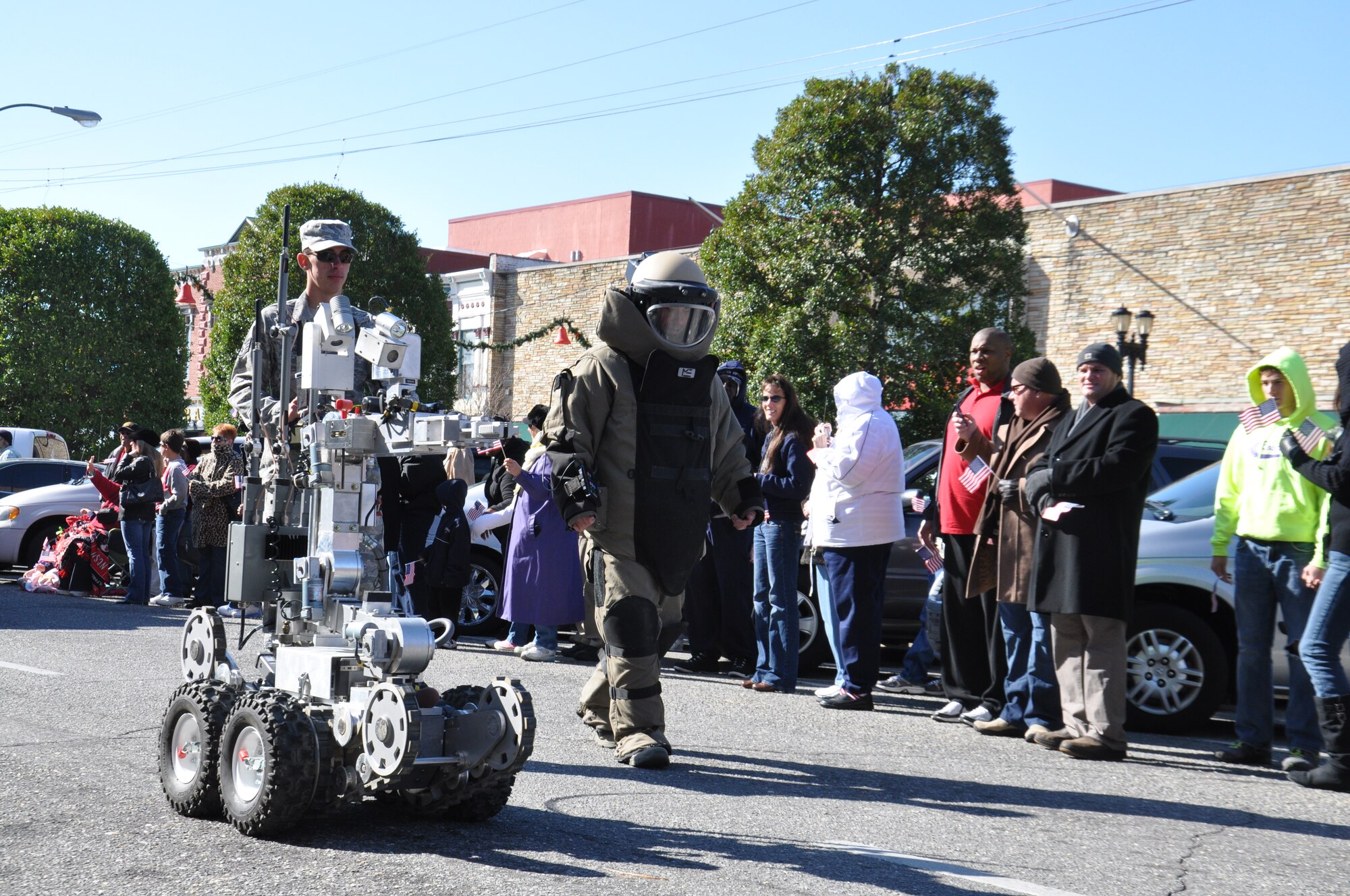 A 4th Civil Engineer Squadron explosive ordnance disposal (EOD) flight specialist controls the F-6 Alspa robot as another EOD member walks in the bomb suit, during the Veteran's Day parade in downtown Goldsboro, Nov. 11, 2011. EOD and community emergency response officials regularly partner to ensure public safety and build morale. (U.S. Air Force photo by Airman 1st Class Mariah Tolbert)