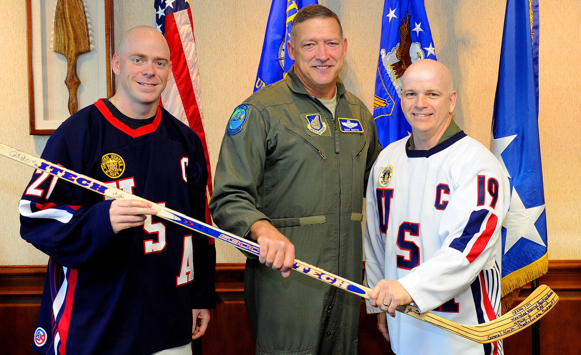 Members of the Warriors for Warriors organization present Pacific Air Forces Commander Gen. Gary North with a hockey stick here on Nov. 17.  All members of the hockey league signed the hockey stick, and it was presented by U.S. Navy Master-at-Arms 1st Class David Taylor (left), Leading Petty Officer for the base security department and president of Warriors for Warriors, and U.S. Air Force Lt. Col. Tom Bell (right), U.S. Pacific Command J33 current operations and vice president of Warriors for Warriors.  Warriors for Warriors is a sports organization designed to help raise funds and awareness for wounded service members.  The group recognized Gen. North for his support and participation in the ceremonial puck drop during the annual Wounded Warrior charity hockey game Aug. 28. MA1 Taylor, captain of the Navy-Marine-Coast Guard Team, and Lt. Col. Bell, captain of the Army-Air Force Team, helped raise $15,000 this year by coordinating the annual hockey game comprised of service members from all branches assigned to the island of Oahu.  (U.S. Air Force photo/Tech. Sgt. Jerome S. Tayborn/Released)
