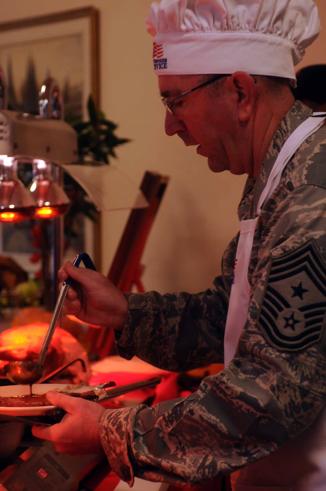 Chief Master Sgt. Jeffrey Craver, 31st Fighter Wing command chief, serves a meal  Nov. 24 at La Dolce Vita Dining Facility on Aviano Air Base, Italy. The dining facility staff prepared a holiday meal while base leadership volunteered to serve Airmen and their families. (U.S. Air Force photo/ Airman 1st Class Jenay Randolph)   