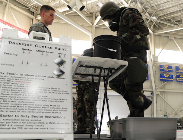 Senior Airman Ross Kreikemeier watches as a mock deployer demonstrates his ability to perform decontamination correctly during the Ability To Survive and Operate Rodeo at Nose Dock One at Joint Base Charleston - Air Base Nov. 28. The rodeo was held to help prepare more than 700 Airmen for the upcoming JB Charleston Operational Readiness Inspection. The rodeo included  Self Aid Buddy Care, weapons familiarization, Unidentified Explosive Objects training and donning chemical protection gear. Kreikemeier is from the 628th Civil Engineer Squadron   (U.S. Air Force photo/ Staff Sgt. Nicole Mickle)  