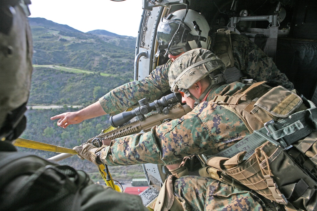 Gunnery Sgt. Jakub Biziorek, the platoon sergeant for the sniper platoon, Headquarters and Support Company, 2nd Battalion, 1st Marine Regiment, listens to his spotter as he points out different targets for him to sight in on while flying in a Navy Sikorsky HH-60H Rescue Hawk over Camp Horno, Nov. 29.  The spotters learned the importance of communication from this type of training because they have to be in constant contact with the shooter, crew chief and pilot to give the shooter the best opportunity for accuracy.