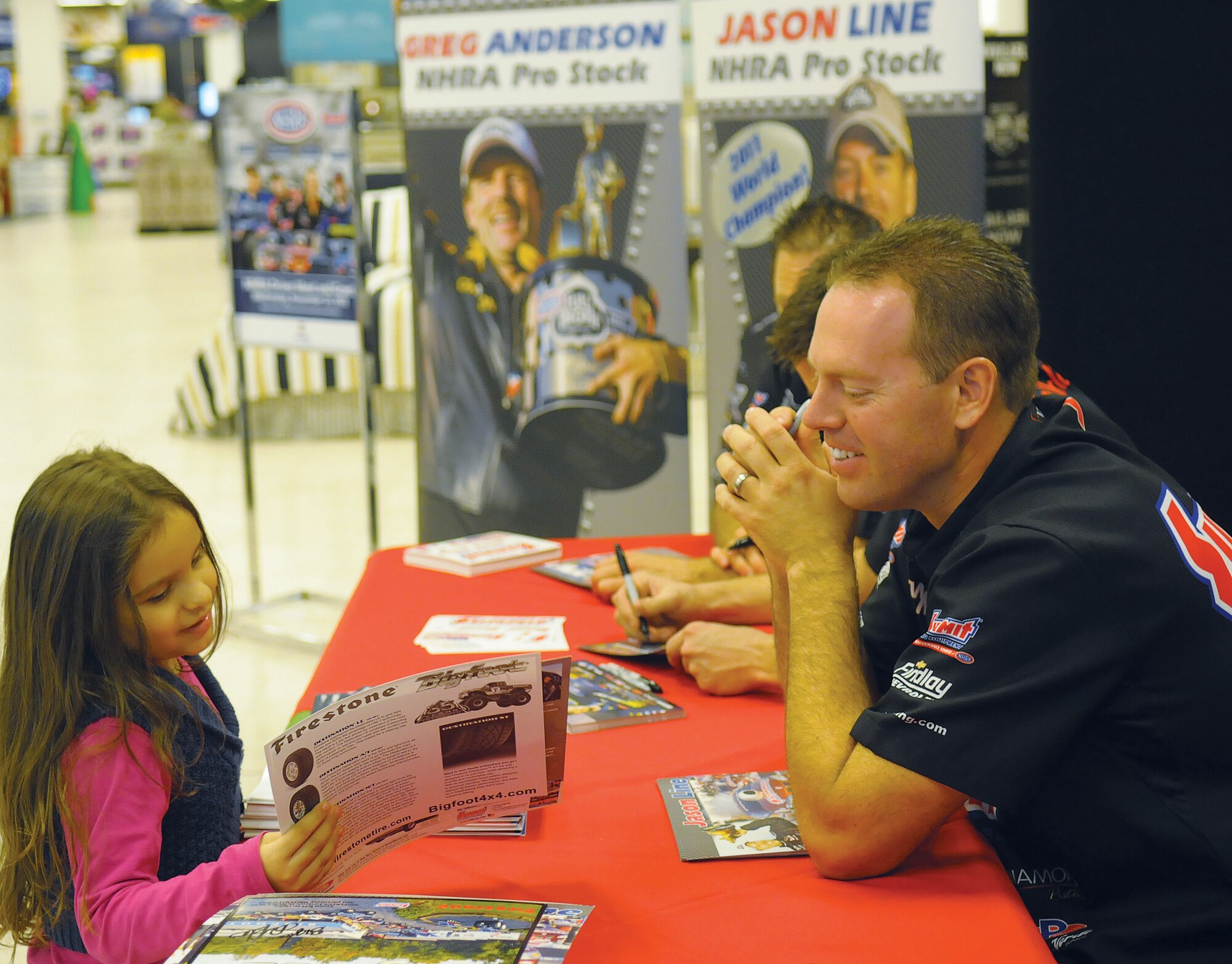Jason Line, 2011 National Hot Rod Association champion, smiles after handing a pint-sized fan a signed, personal autograph during his visit here at the Kaiserslautern Military Community Center, Nov. 23, 2011. Line along with three other NHRA members came to Germany to visit troops and say thank you. This is the seventh time members of the NHRA have toured Germany in honor of the troops as part of their annual tour sponsored by Armed Forces Entertainment. (U.S. Air Force Photo by Staff Sgt. Travis Edwards)