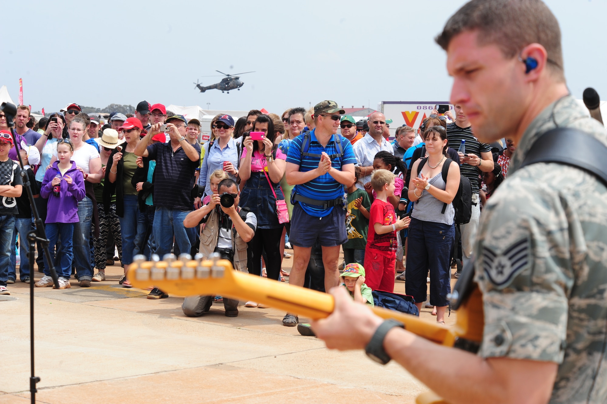 PRETORIA, South Africa - Staff Sgt. Dustin Trimble, U.S. Air Forces Europe Band “Touch ‘n Go” lead guitarist performs while visiting South Africans look on and an aerial demonstration is shown in the distance during the 2011 Air Show & Lifestyle Expo at Waterkloof Air Force Base, Oct. 1. The band performed two one-hour sets, which drew crowds that danced, sang and enjoyed some good old rock and roll music. (U.S. Air Force photo by Tech. Sgt. Todd Wivell)