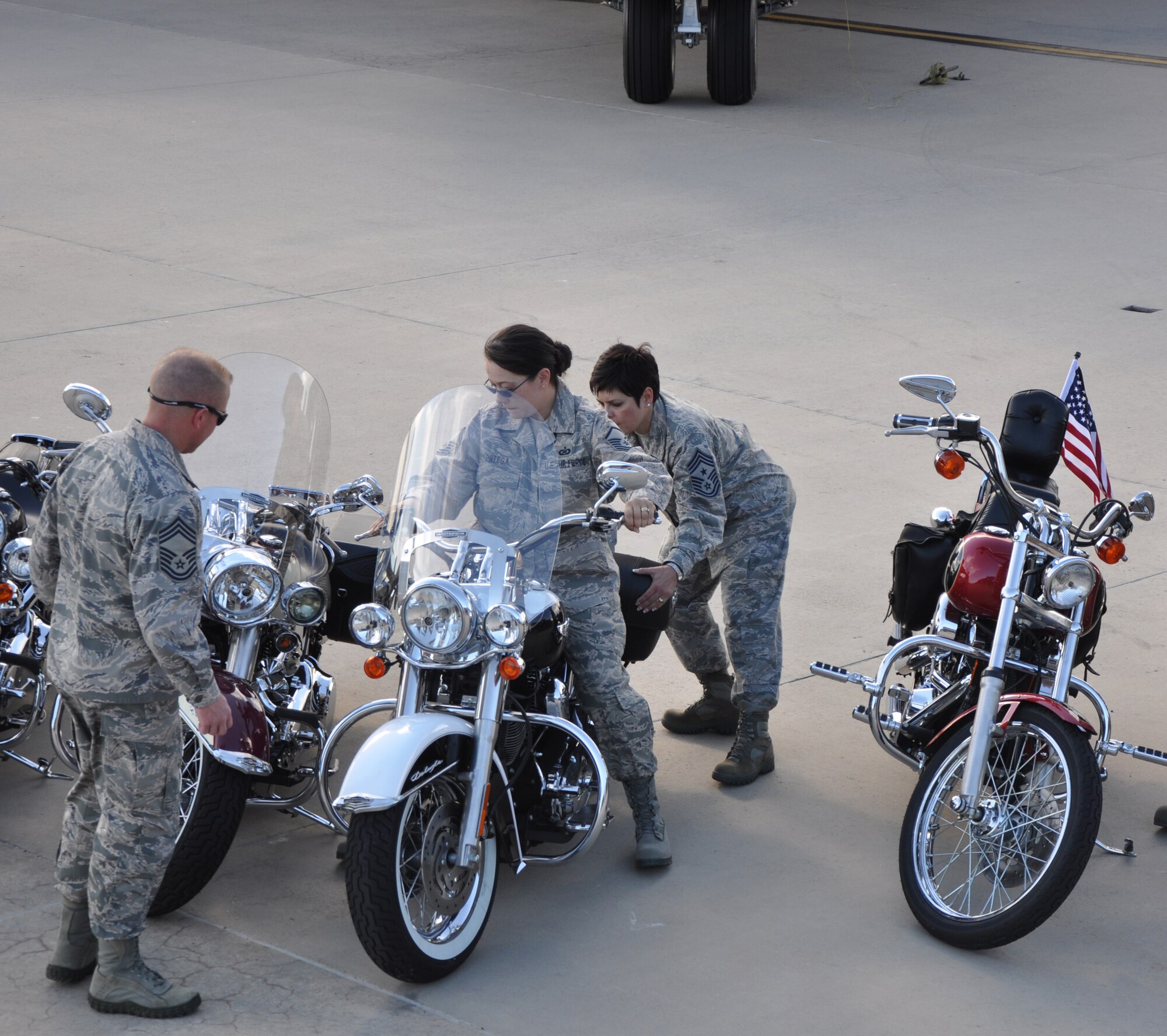 302nd Airlift Wing's Command Chief Suzette Cherry follows direction from her husband Chief Robert Cherry as she helps Master Sgt. Maria Ortaga, 34th Aeromedical Evacuation Squadron maneuver her bike into position. Members of the 302nd Airlift Wing and the 731st Airlift Squadron motored their bikes onto the flight line for the first "Hercs and hogs" event.  On Oct. 1, after duty hours the "Airmen bikers" gathered in front of a mighty Herc for a photo opportunity that showcased their love of their bike and their love of the C-130. (U.S. Air Force photo/Tech. Sgt. Peter Dean)
