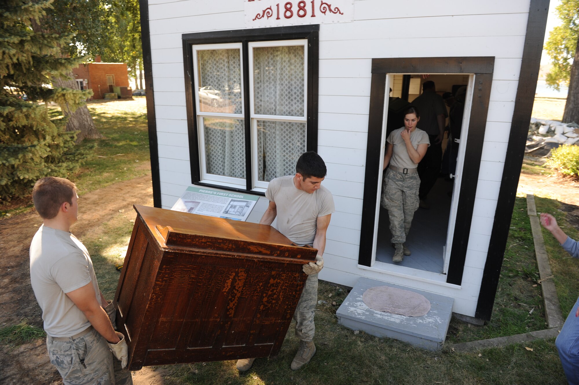 Cadets 1st Class Cody Main, left and Nathan Timsuren, move furniture into Pierre’s first school house, to get the facility ready to accept visitors, while Cadet 2nd Class Cassandra Hill moves to get out of the doorway to bring more materials into the school house.. (U.S. Air Force Photo/John Van Winkle)
