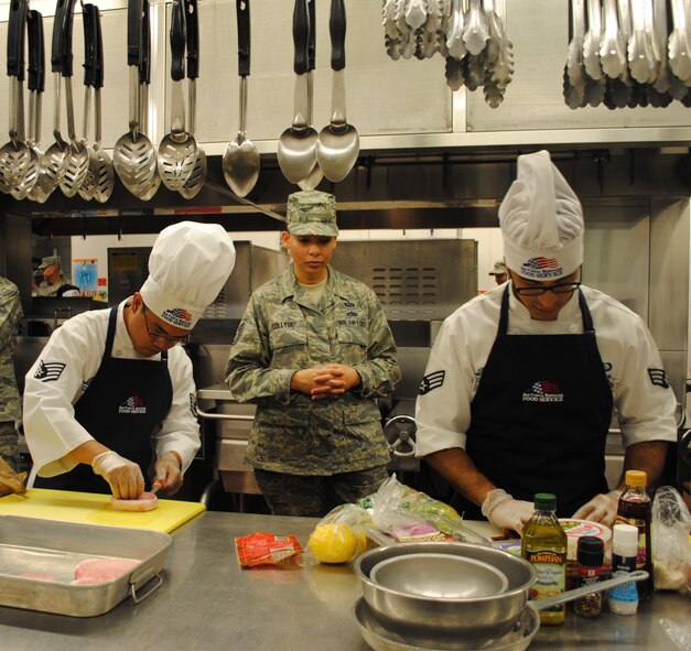 Staff Sgt. Christopher Bactad and Senior Airman Josue Silva, missile chefs with the 490th Missile Squadron, prepare a dish during the 2nd Quarter Warrior Chef Competition as Tech. Sgt. Kimberly Collyge, a judge, watches. The duo’s stuffed pork chops became the eventual winning dish. (U.S. Air Force photo/Katrina Heikkinen)