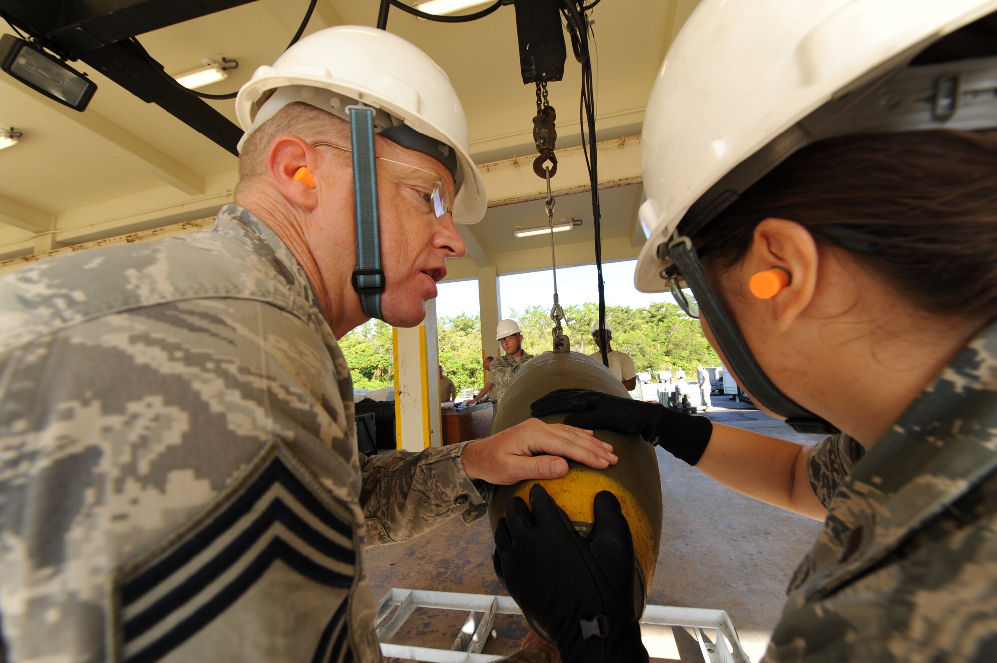 United States Air Force Chief Master Sgt. Robert Benton, 18th Munitions Squadron chief of munitions, and 2nd Lt. Marie Ramirez, 18th Logistics Readiness Squadron war reserve material officer, guide Mark 83 bomb bodies into a harness during an ammo orientation in the munitions area at Kadena Air Base, Japan, Sept. 30. Commanders and leaders from the base were given the opportunity to learn common munitions skills in order to see what a typical munitions Airman goes through during contingency and exercise operations. (U.S. Air Force photo/Airman 1st Class Jarvie Z. Wallace)