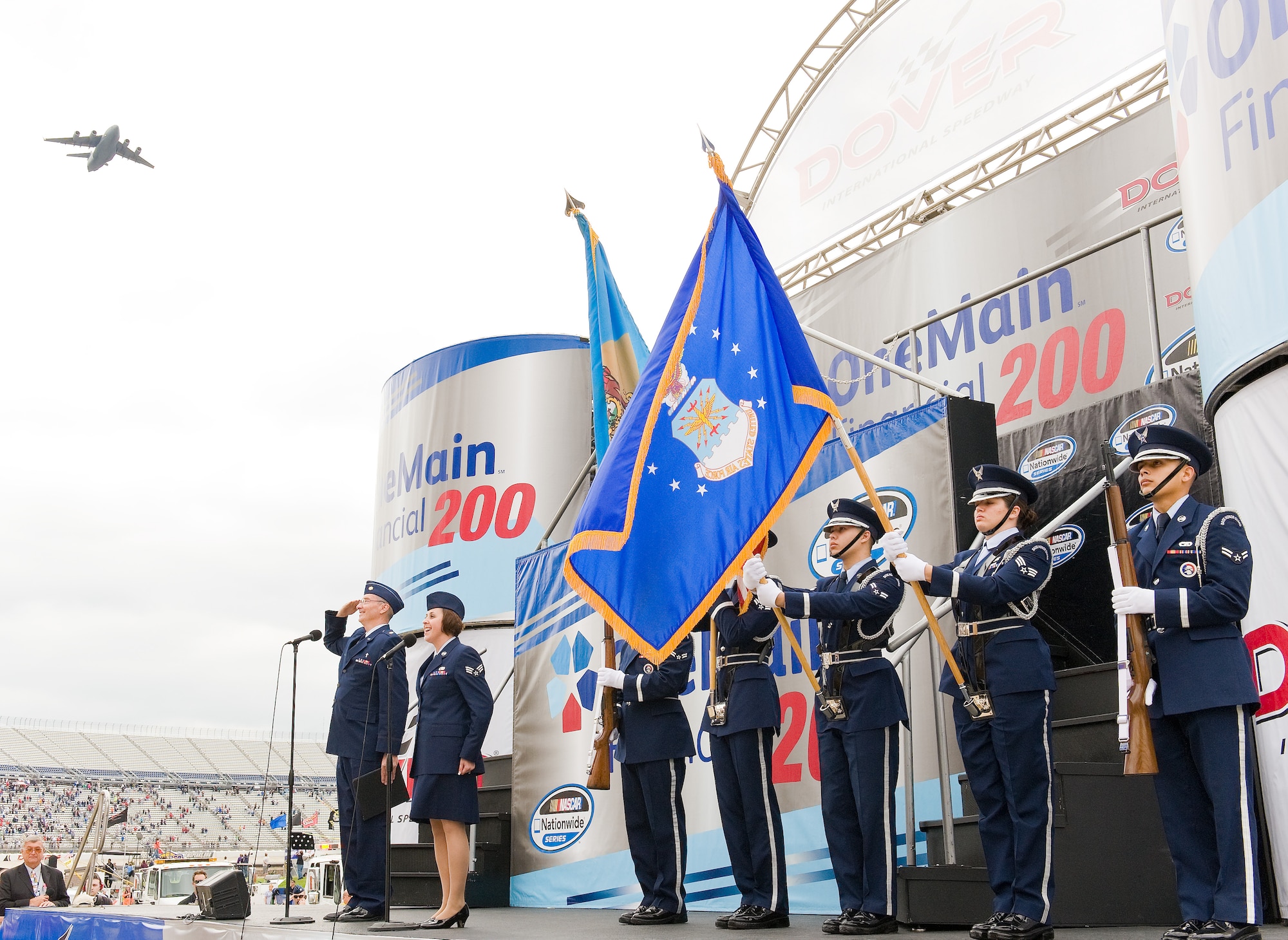 Senior Airman Naomi Scott, 436th Maintenance Squadron, sings the national anthem as a C-17 Globemaster III from Dover Air Force Base, Del., flies overhead Oct. 1, 2011, at Dover International Speedway in Dover, Del. Maj. Timothy Hirten, a chaplain with the 436th Airlift Wing, and the Base Honor Guard pay respect to the Colors prior to the OneMain Financial 200 NASCAR Nationwide Series race. (U.S. Air Force photo by Roland Balik)