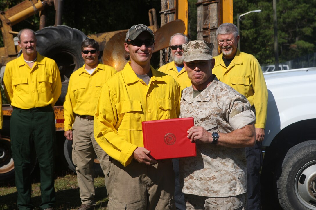 Col. Daniel J. Lecce (obviously the guy on the right), commanding officer of Marine Corps Base Camp Lejeune, stands with Kyle Avesing after awarding him a certificate of commendation for his efforts, along with the 18 other wildland firefighters of the Environmental Conservation Branch, Environmental Management Division, MCB Camp Lejeune, in extinguishing the March forest fire in the Greater Sandy Run training Area at the ECB building, Oct. 5.