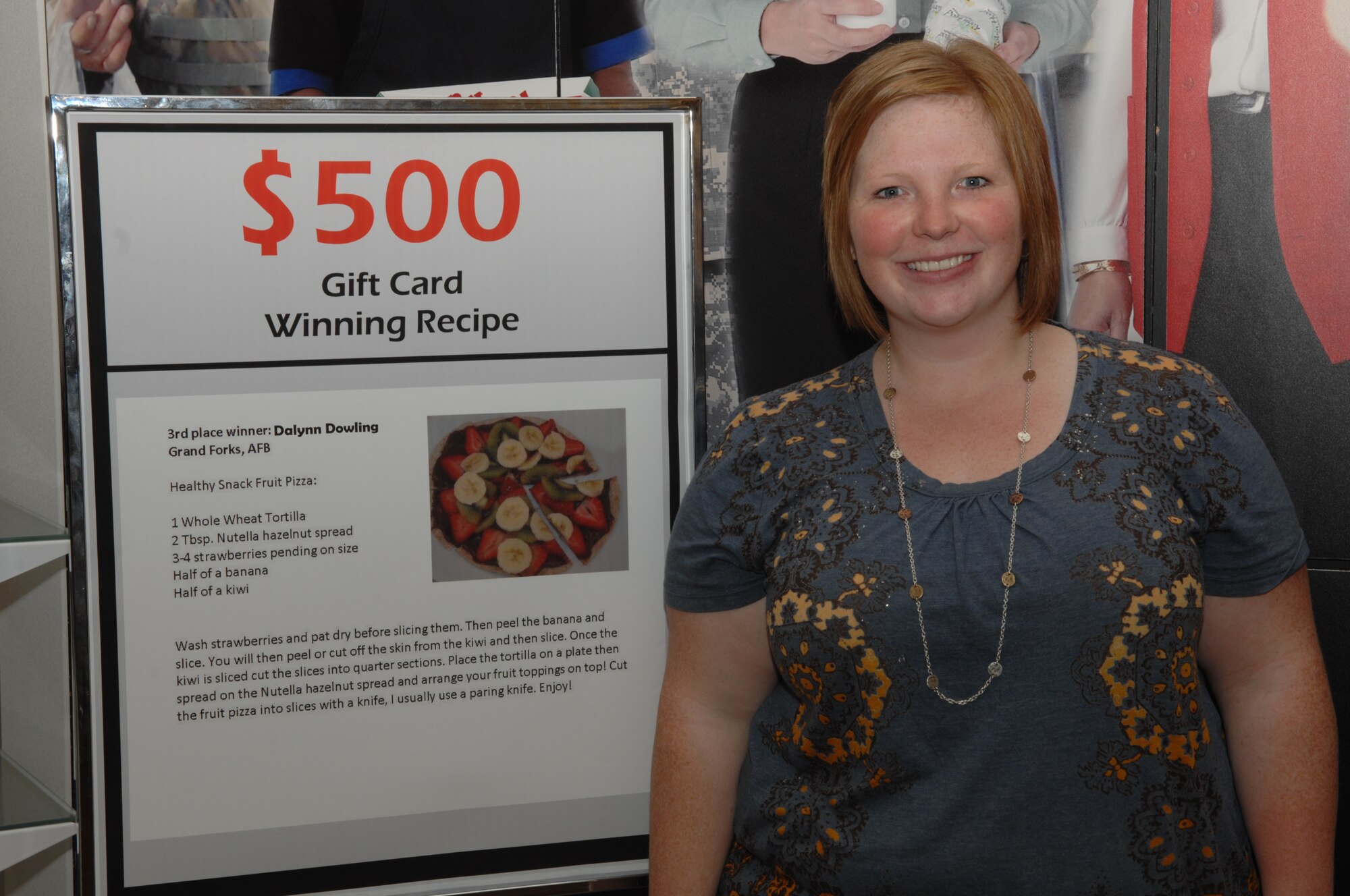 Dalynn Dowling, wife of Staff Sgt. William Dowling, 319th Communications Squadron, poses next to her healthy snack recipe on Grand Forks Air Force Base Oct. 5.  Mrs. Dowling received a $500 gift card for her healthy snack fruit pizza recipe.  (U.S. Air Force photo by Airman 1st Class Ashley N. Taylor)