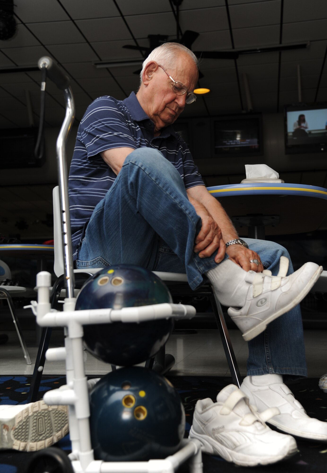 Sitting next to his custom-designed ball carrier made out of PVC pipe, Bernard Moyer changes into his bowling shoes at Gaudé Lanes.  (U.S. Air Force photos by Airman 1st Class Heather Heiney)