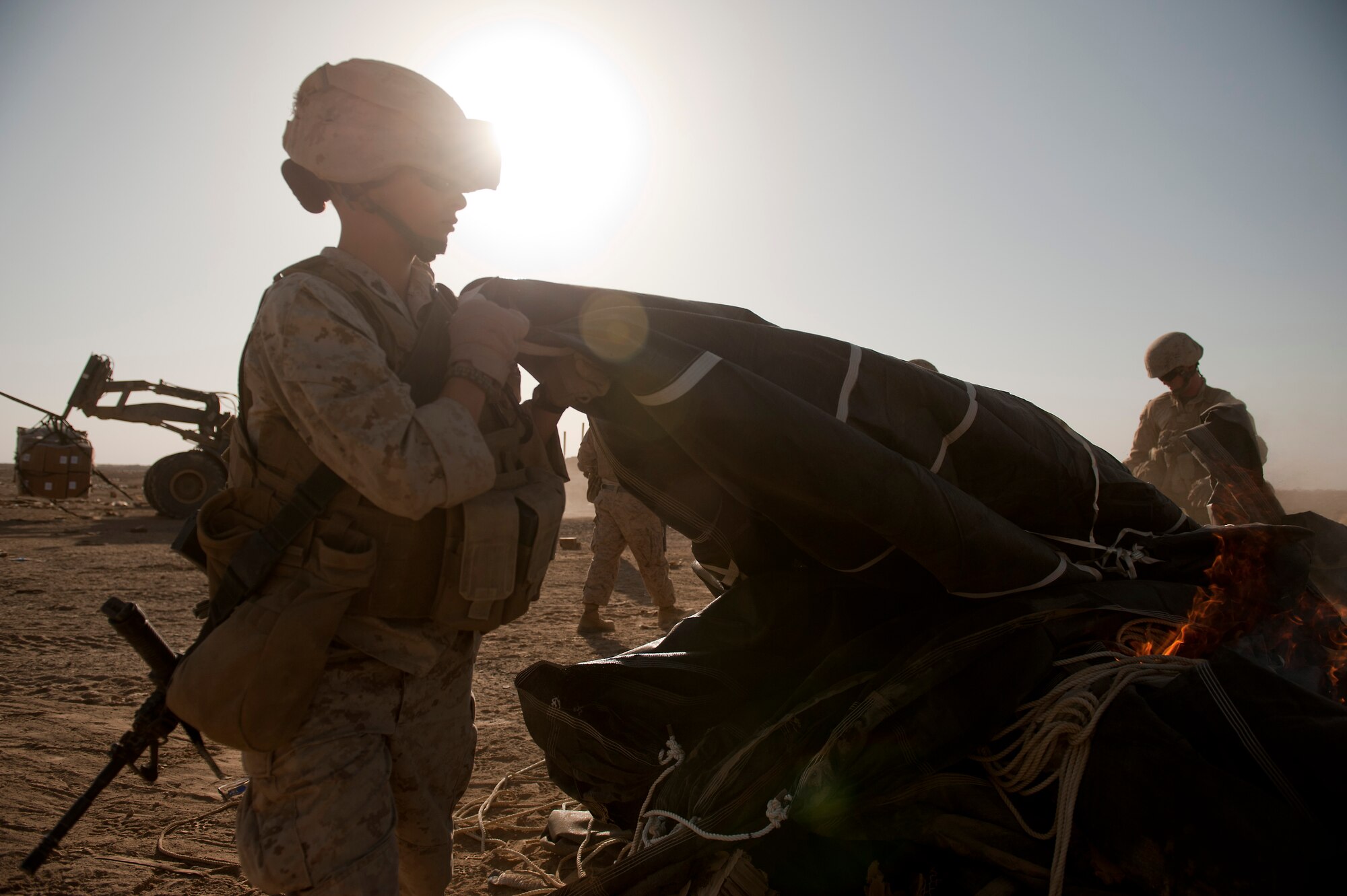 U.S. Marine Corporal Alexandra Melnick, 2nd Battalion, 4th Marines of the 5th Marine Regiment, sets a parachute used during an aerial delivery of food rations on to a fire on Oct 3, 2011.  The parachutes and other packing material are collected and burned on site to reduce the debris left on the drop zone. Aerial delivery of food and water allows Marines to get some critical supplies without having to rely on risky ground convoys.   (U.S. Air Force Photo/Master Sgt. Jeffrey Allen)