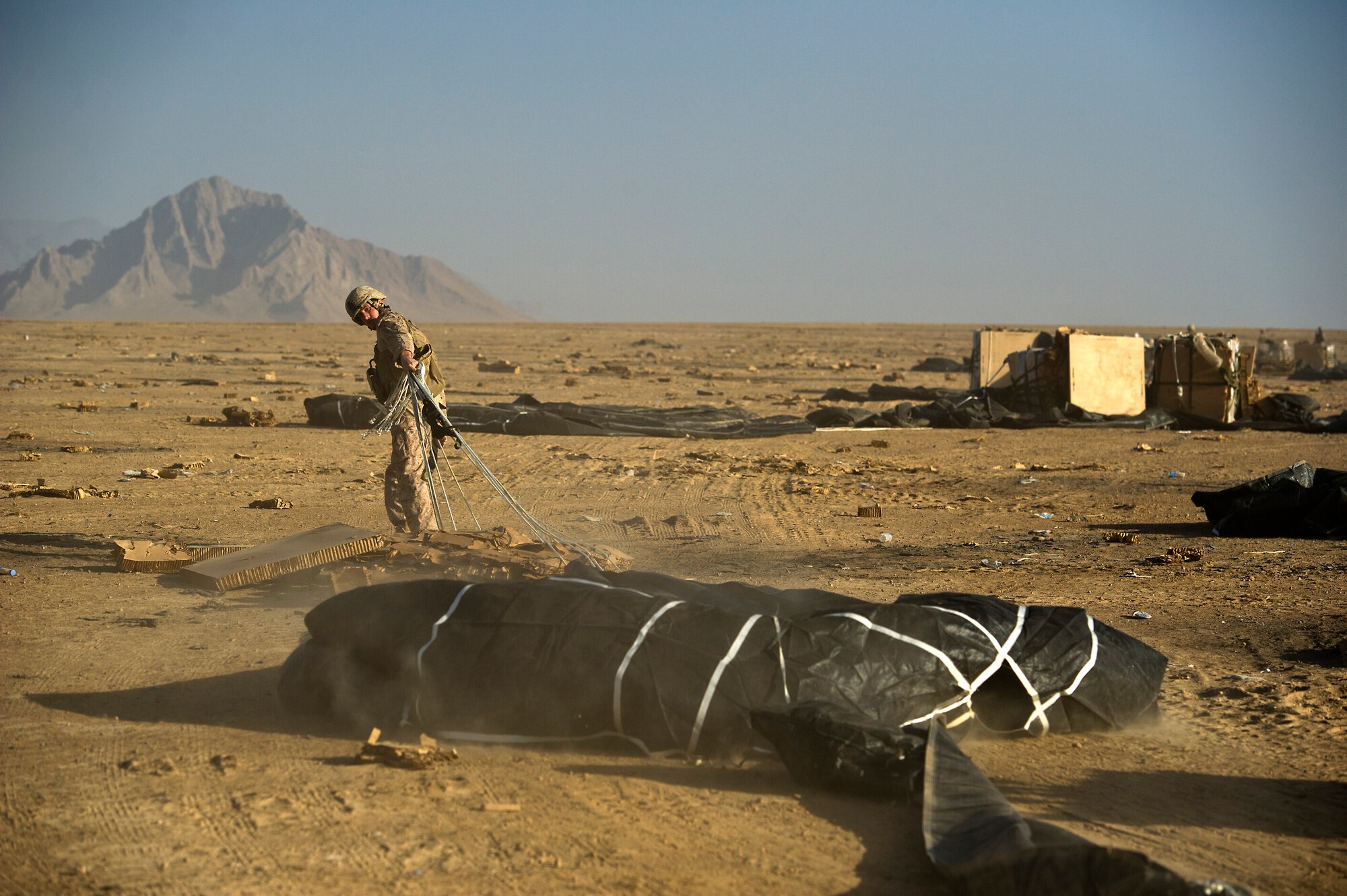 A U.S. Marine drags a parachute away from a bundle of food rations that were airdropped to Forward Operating Base Edinburgh, the logistics hub for Northern Helmand Province, on Oct. 3, 2011.  The parachutes and other packing material are collected and burned on site to reduce the debris left on the drop zone. Aerial delivery of food and water allows Marines to get some critical supplies without having to rely on risky ground convoys.   (U.S. Air Force Photo/Master Sgt. Jeffrey Allen)