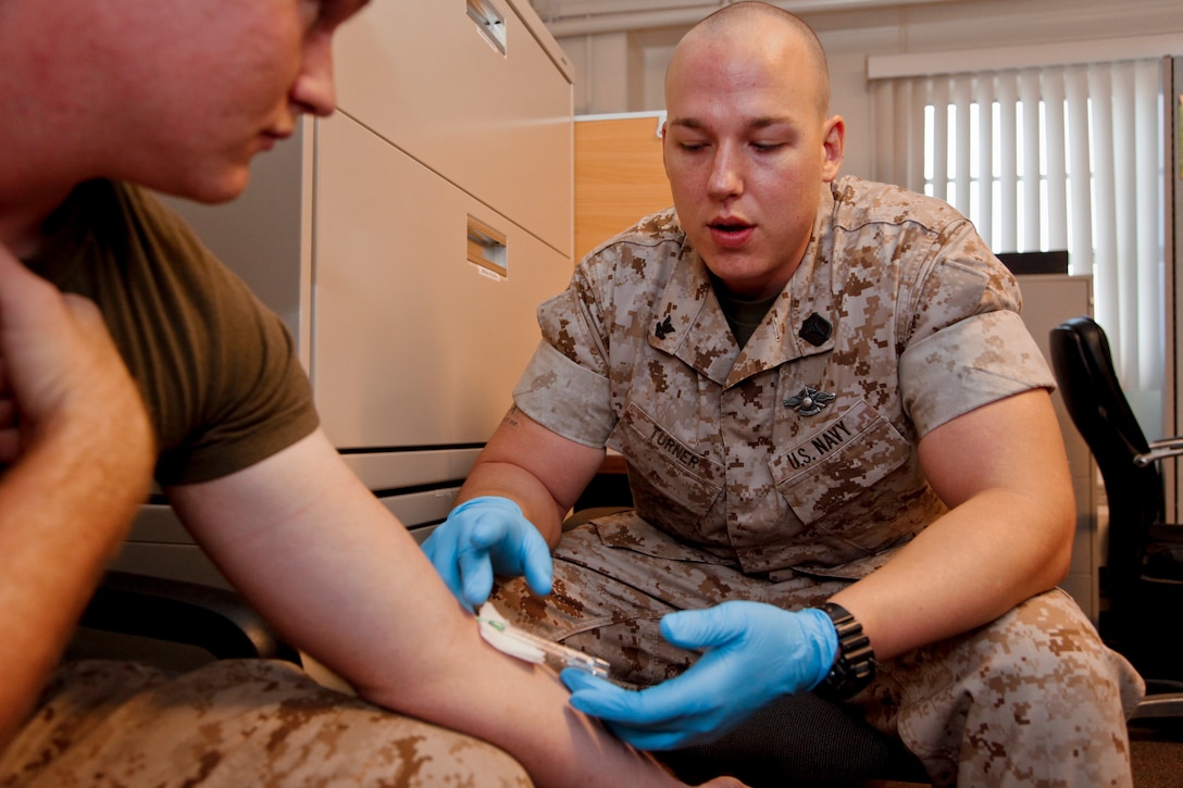 Petty Officer 2nd Class Devin L. Turner, hospital corpsman, 15th Marine Expeditionary Unit Command Element, injects a catheter into Lance Cpl. Philip A. Larkin, an administrative clerk with the unit, at the command post for intravenous therapy, October 5. There are no medical personnel organic to the Marine Corps. For these needs, Marines rely on the Navy’s corpsmen, more commonly referred to as “docs.” As a team they are in charge of meeting the medical needs of 15th MEU personnel. (U.S. Marine Corps photo by Cpl. John Robbart III)