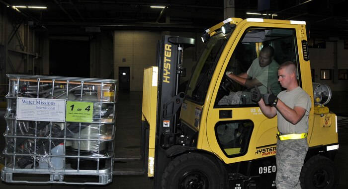Airman 1st Class Brandon Fritz guides Staff Sgt. Michael Shaw while loading a water purification system onto a pallet Oct. 5, at Joint Base Charleston-Air Base. Humanitarian, aid including 20 reverse osmosis water purification systems and two anesthesia machines, will be sent to Colon, Honduras Oct. 25. These supplies will assist more than 20,000 Hondurans in need. Fritz is an air transportation specialist and Shaw is an air transportation journeyman from the 437th Aerial Port Squadron. (U.S. Air Force photo/Airman 1st Class Jared Trimarchi)